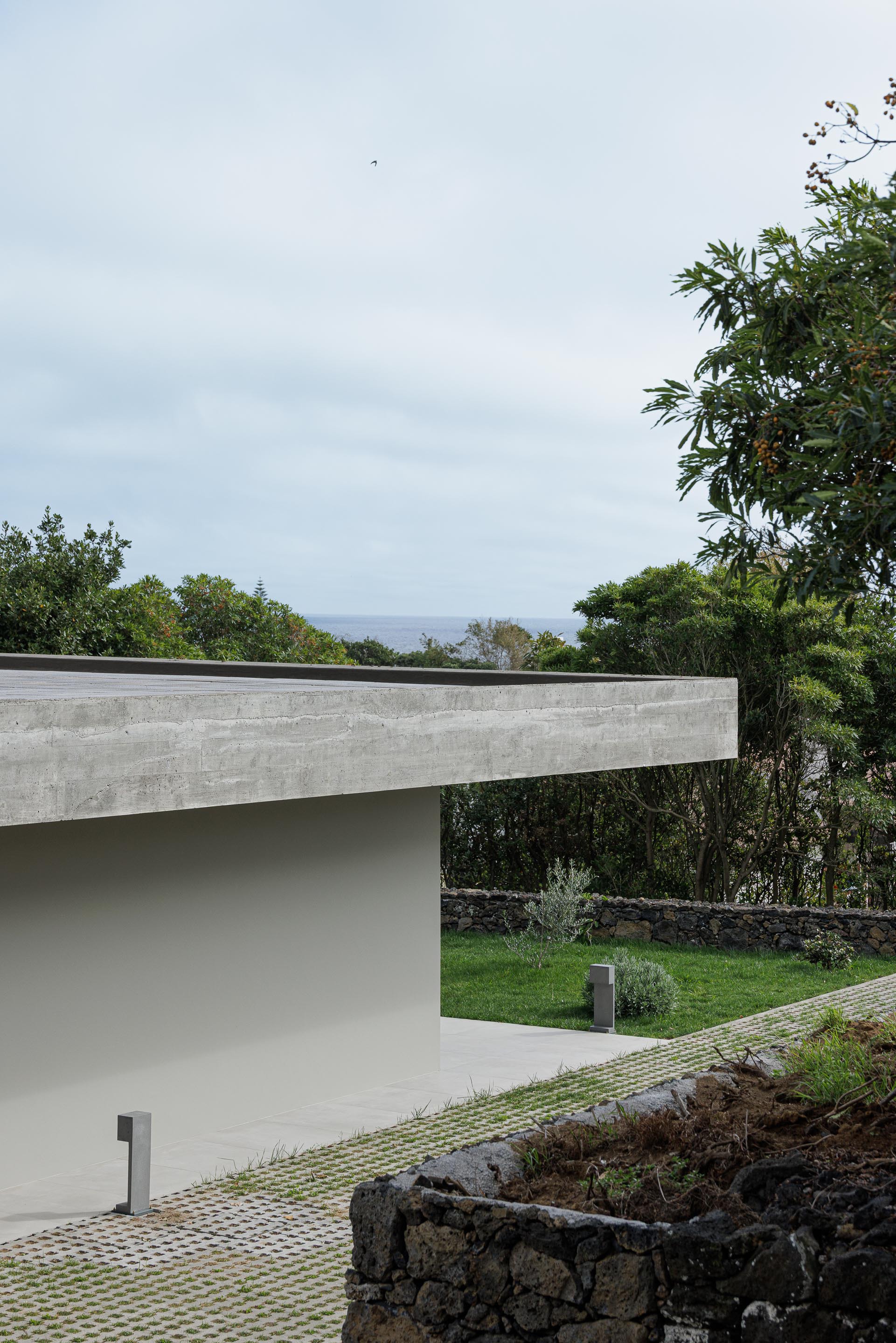 Concrete roof edge projecting over terraced garden with ocean horizon visible through distant vegetation