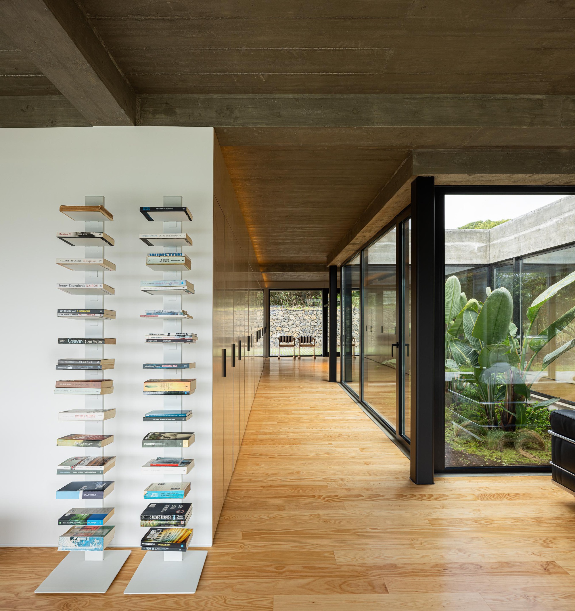 Hallway with floating wall-mounted bookshelves alongside floor-to-ceiling windows framing a tropical garden