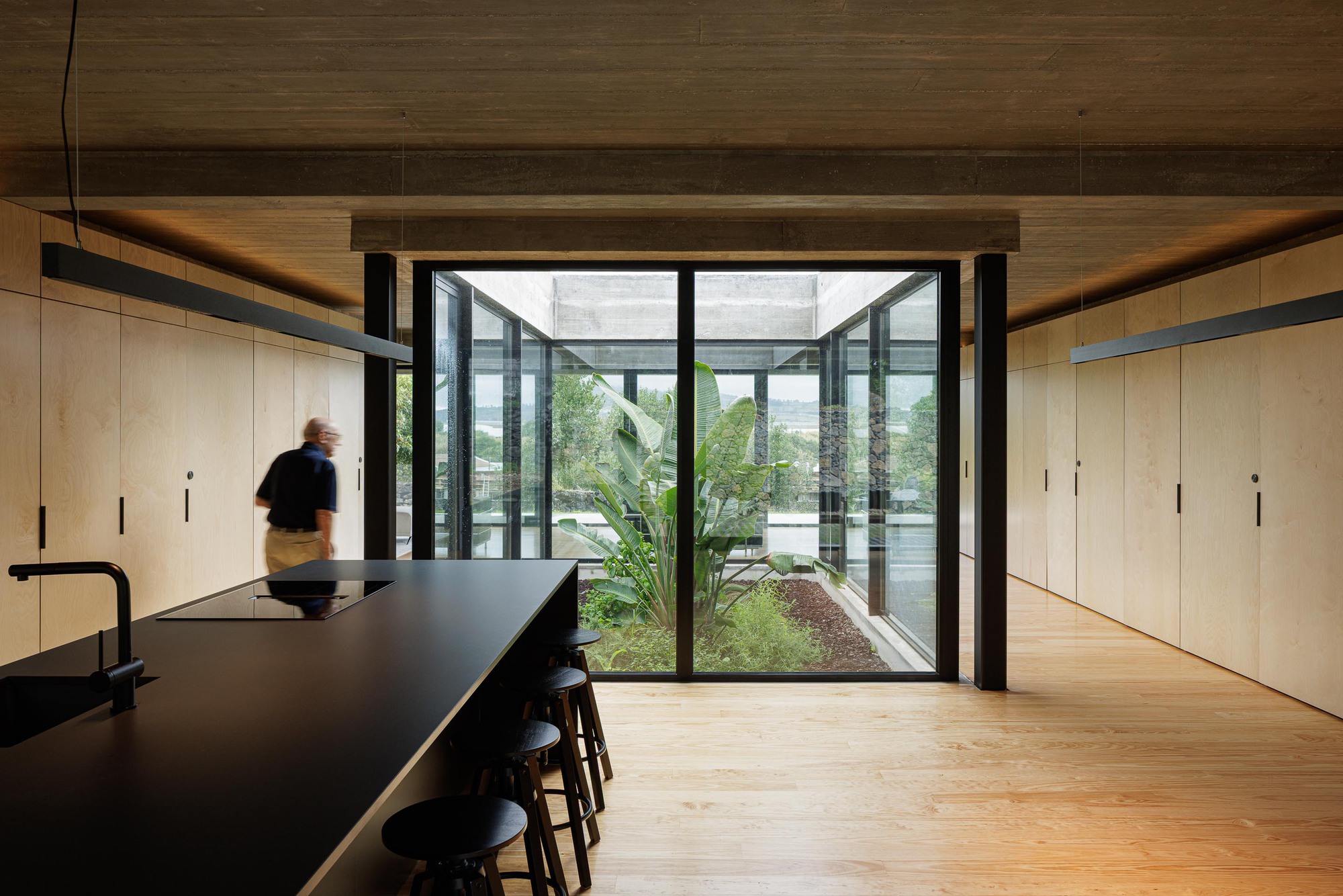 Kitchen opening onto an interior courtyard with timber frame windows and planted garden beds beyond