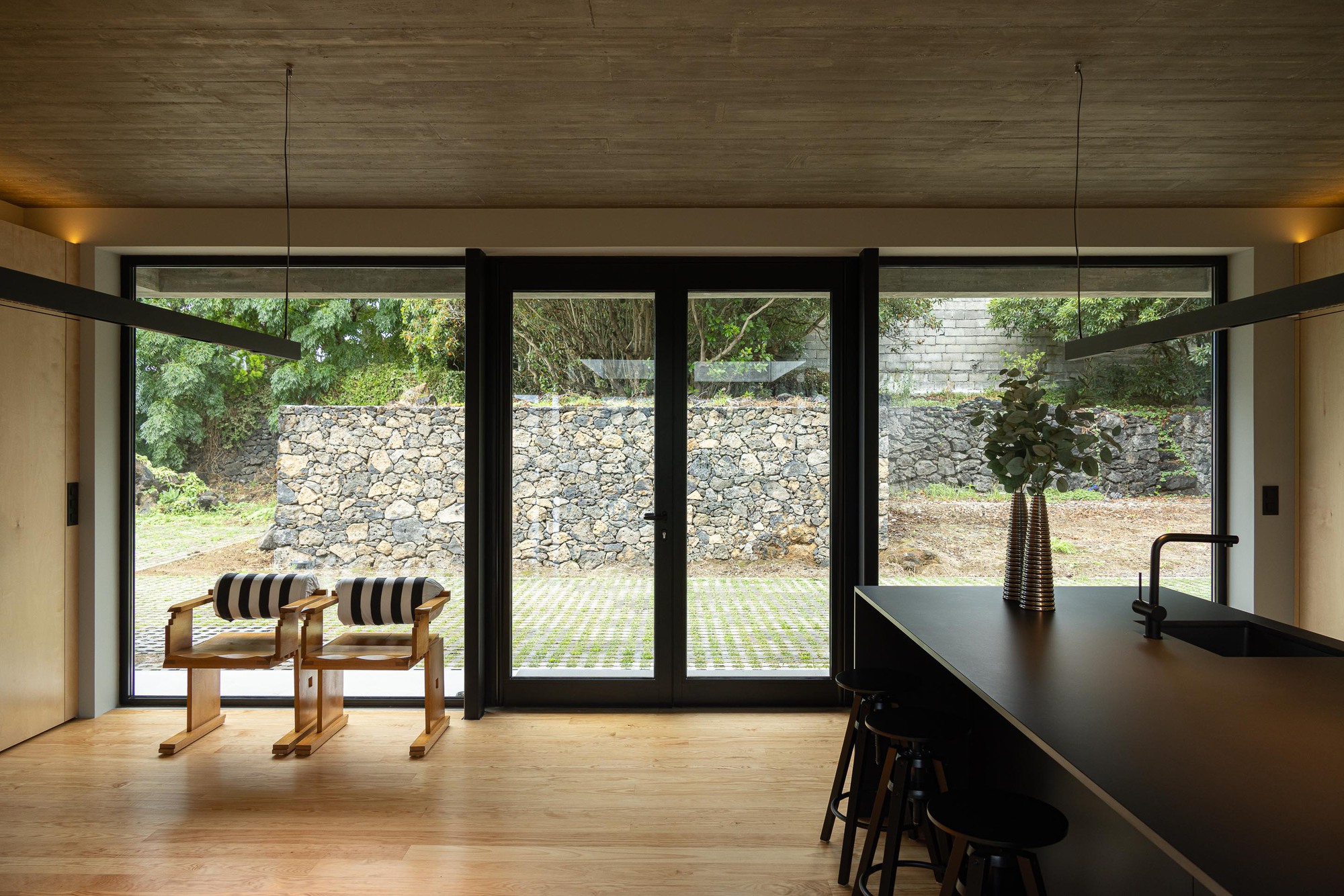 Interior view through black-framed glass doors to a terraced stone retaining wall and garden beyond