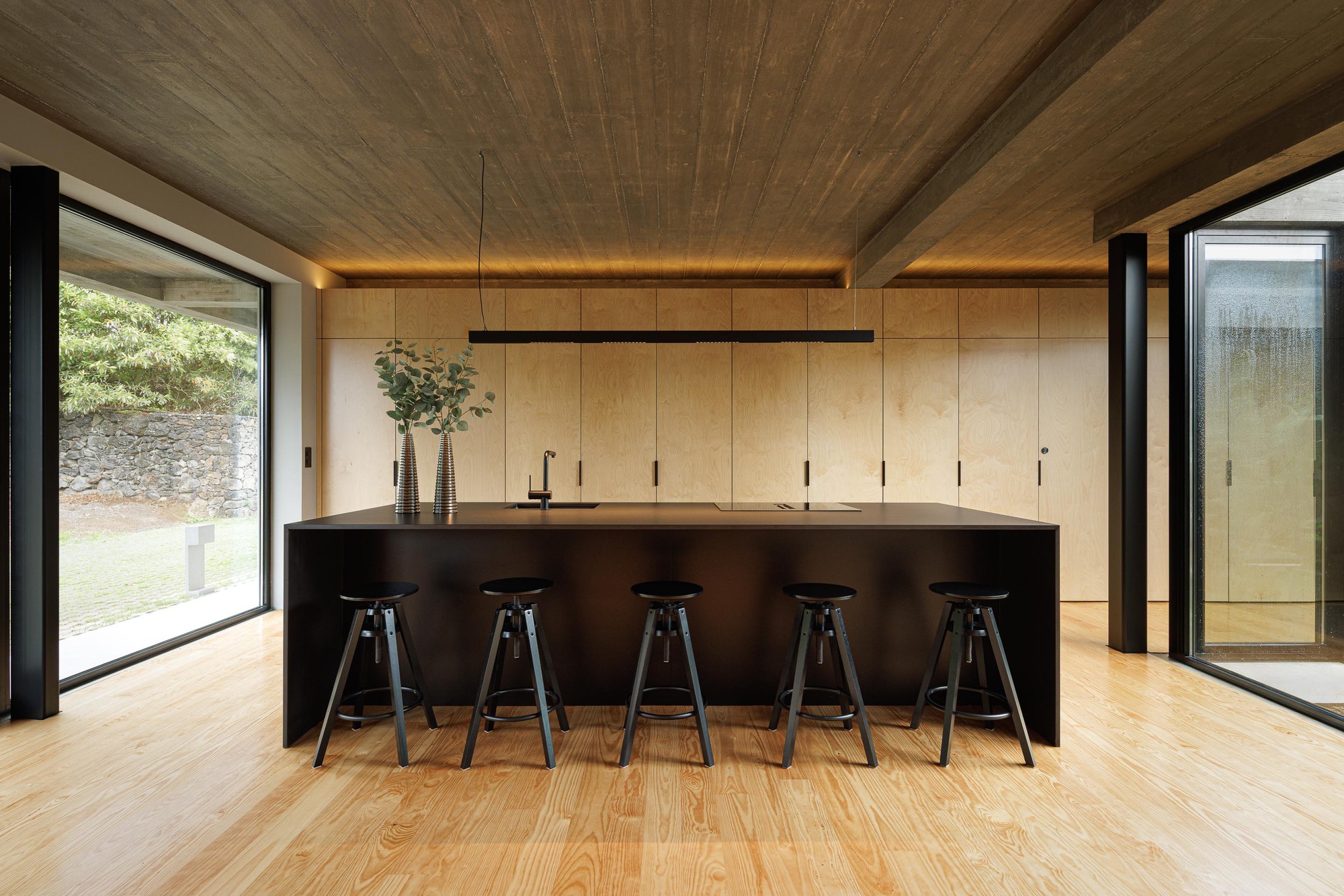 Kitchen island with black metal countertop and five bar stools beneath a wooden plank ceiling