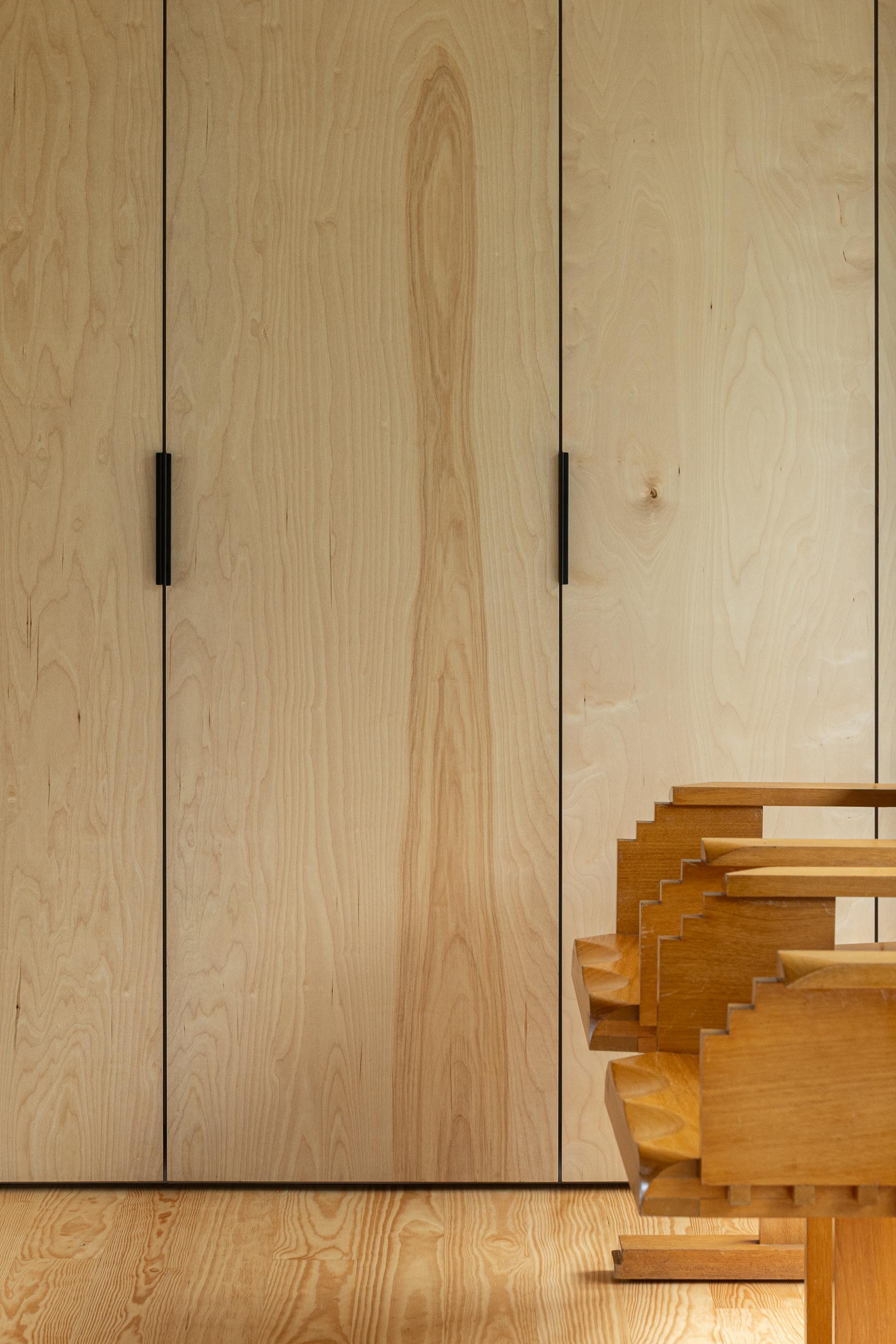 Detail of light plywood panels with black finger pulls beside sculptural timber step element