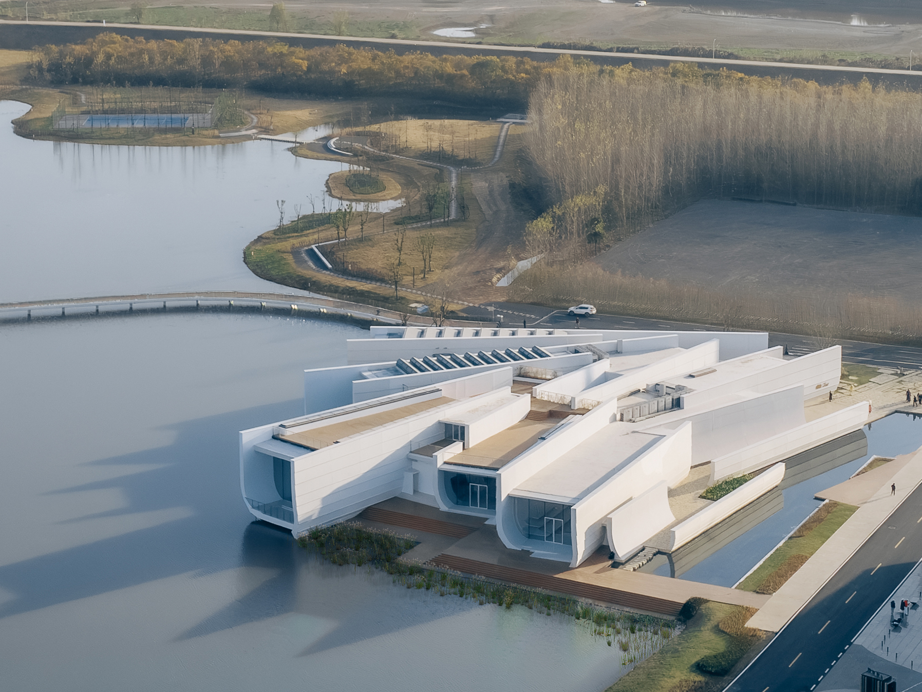 Aerial view of the white angular volumes extending over a lake with bare trees along the shore