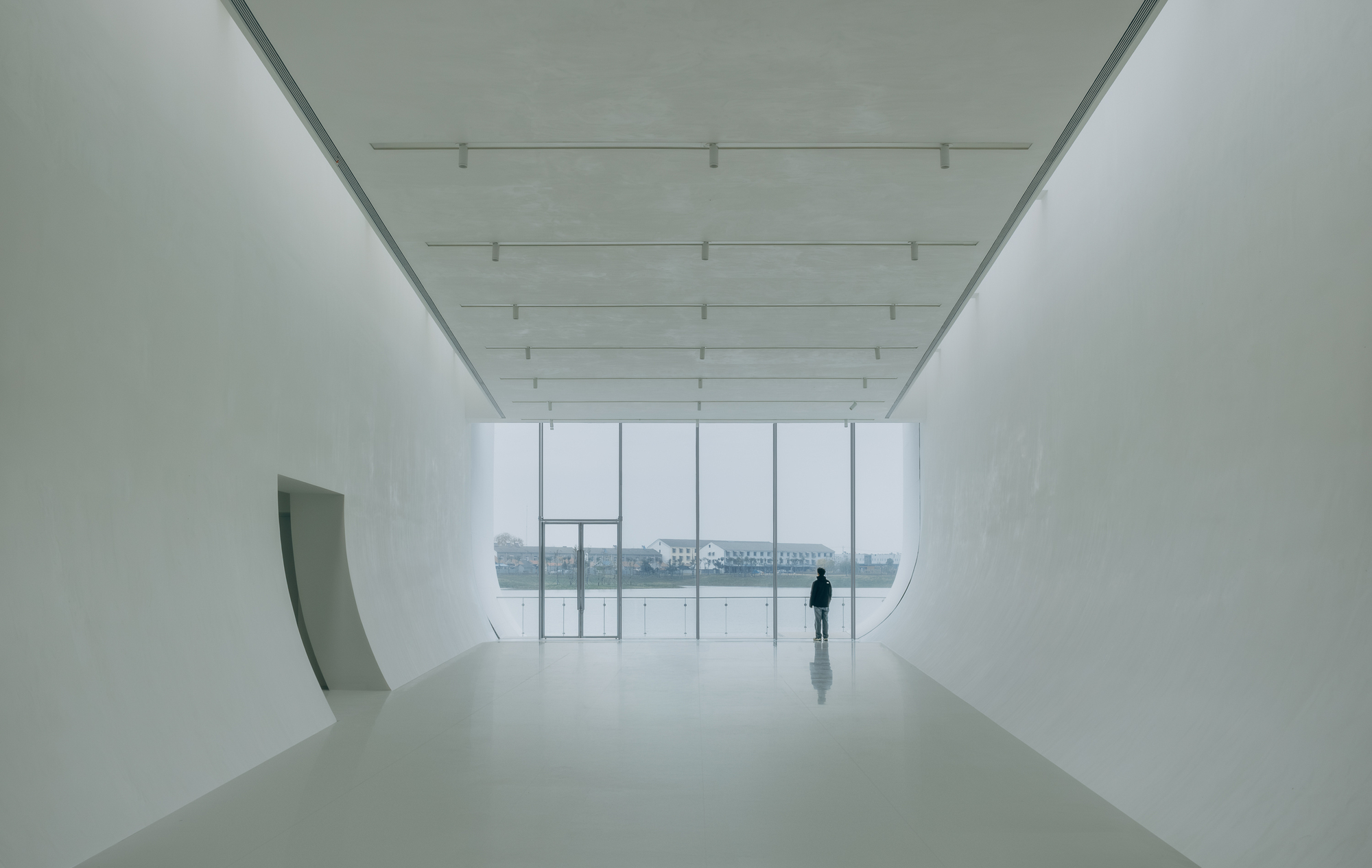 Gallery space with curved white walls and full-height glazing overlooking a misty waterfront