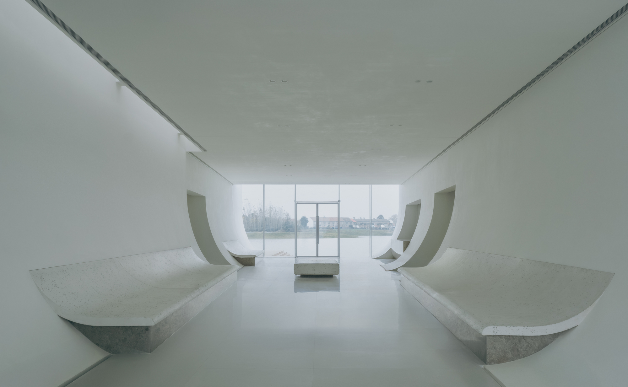 Symmetrical gallery space with paired curved benches flanking glazed wall opening to water view