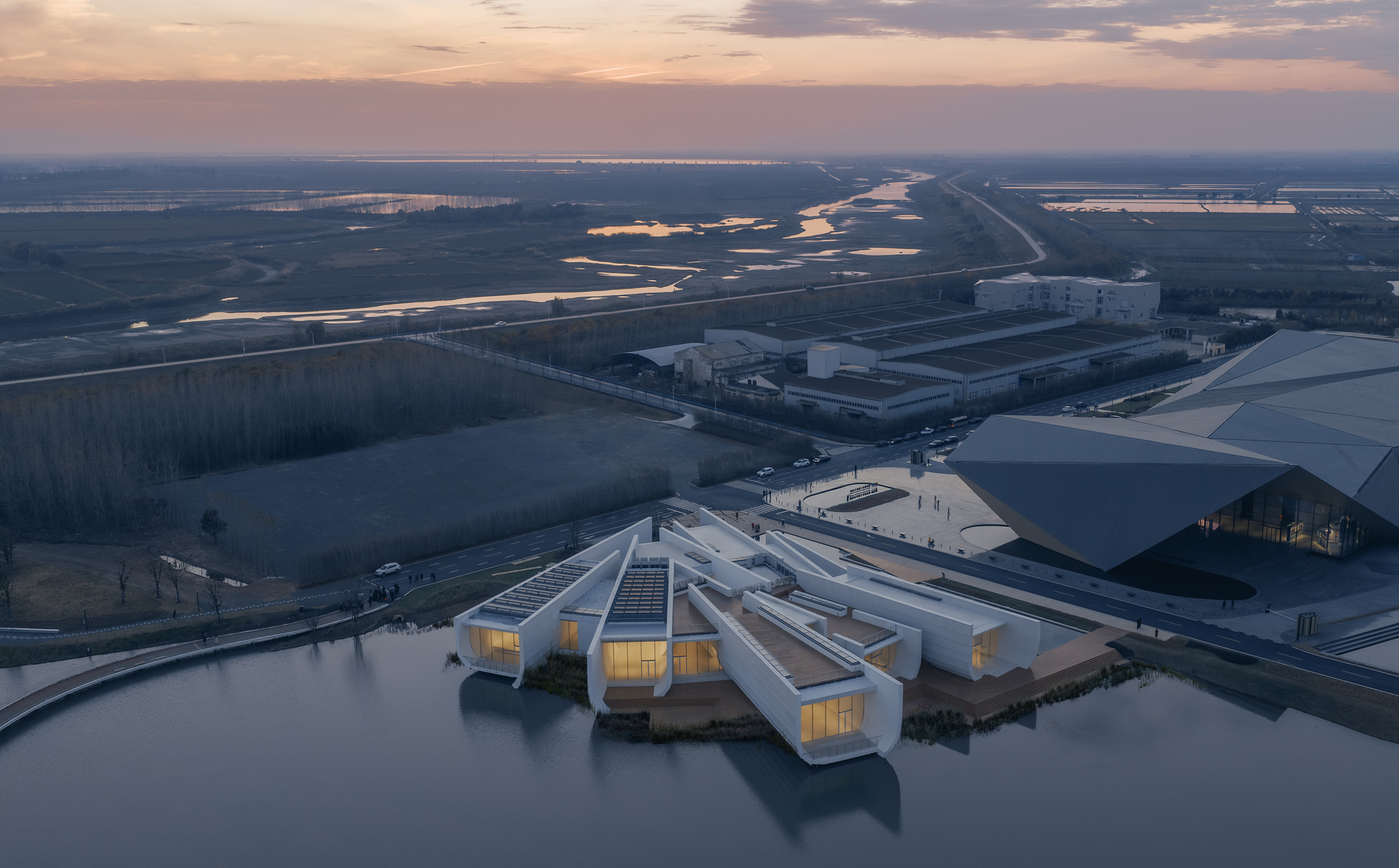 Aerial view of white clustered pavilions with illuminated interiors beside wetlands at dusk