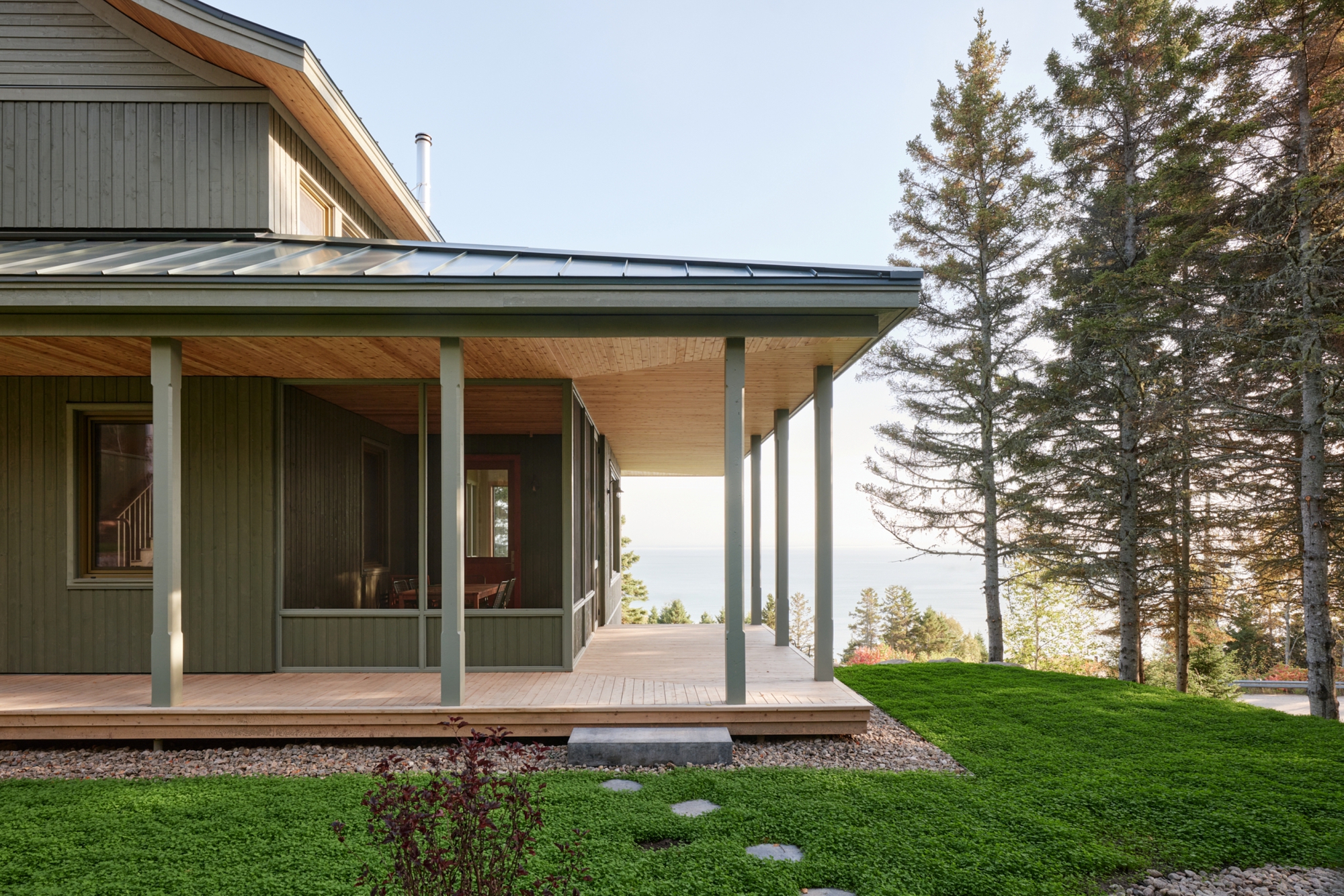 Covered porch with slim steel columns and plywood ceiling overlooking a lawn and distant treeline
