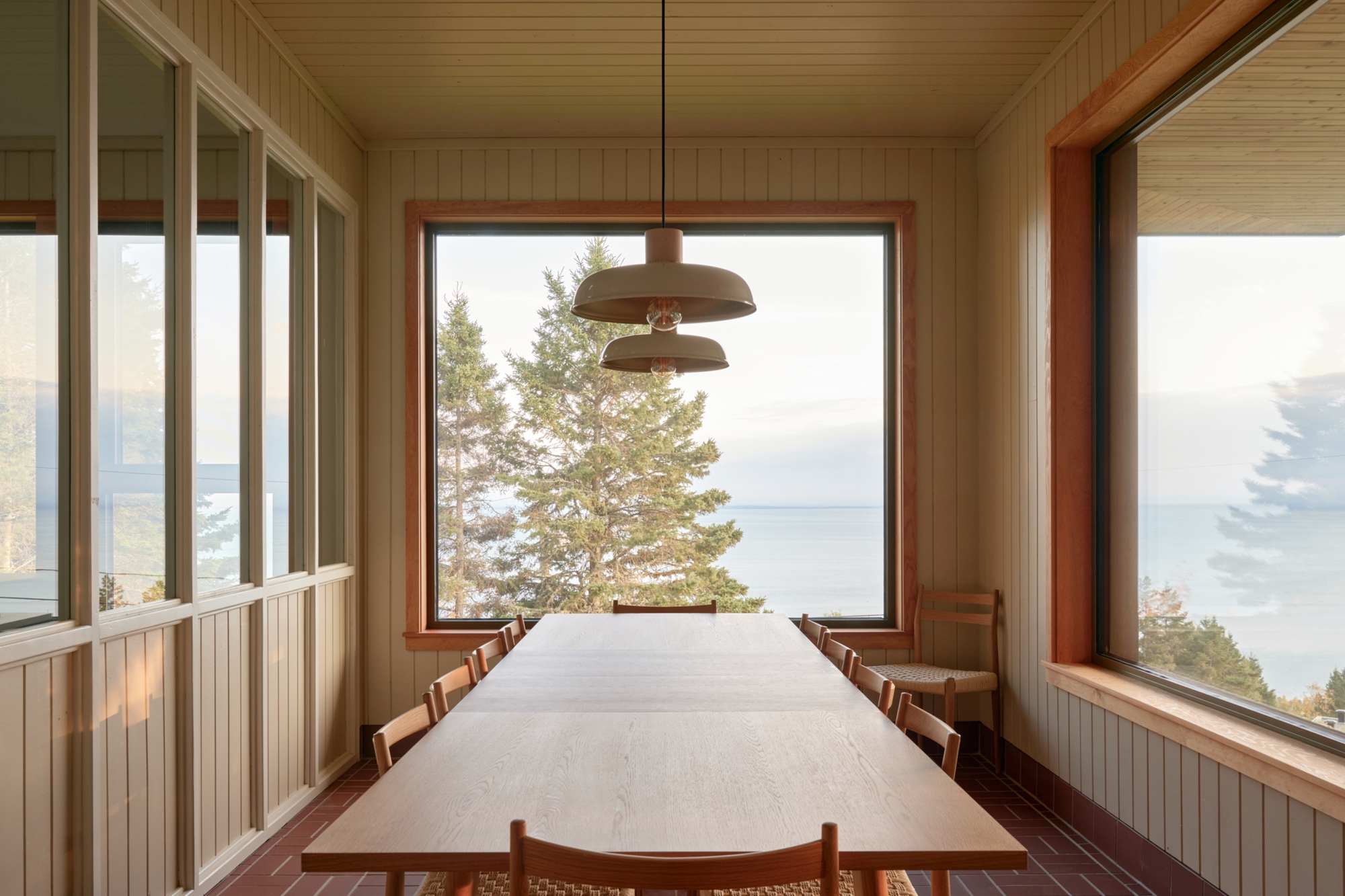 Timber lined dining room with picture window framing a pine tree and distant water view