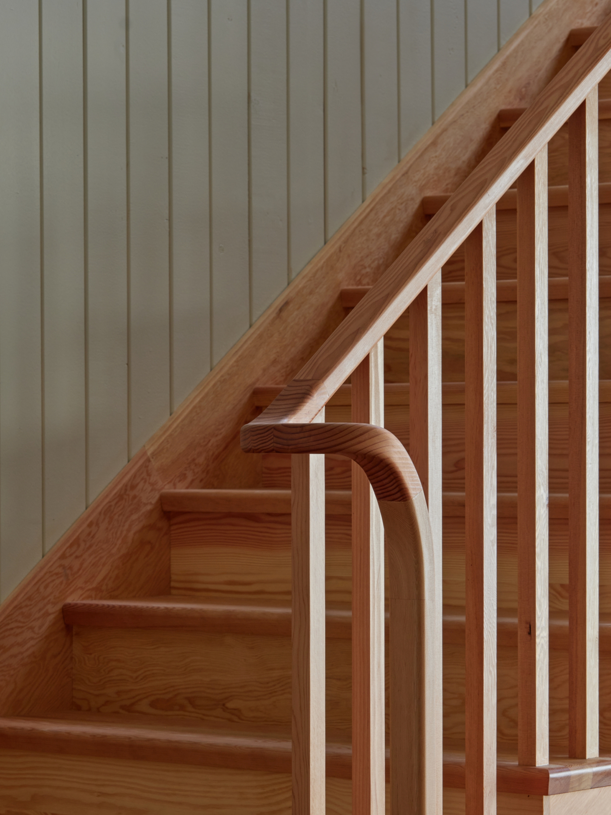 Detail of timber staircase with curved handrail and vertical balustrade against painted panelled wall