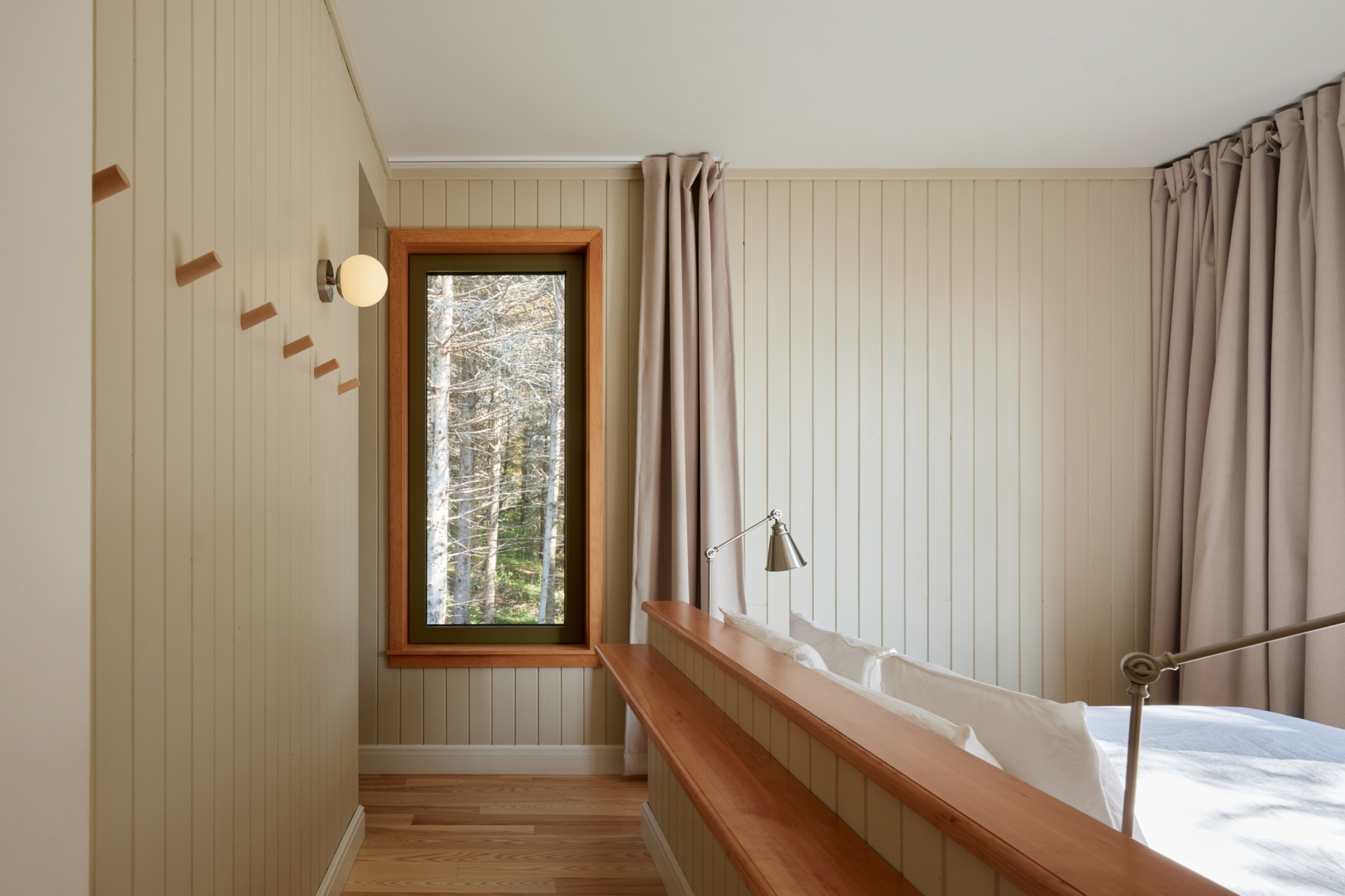 Bedroom with vertical tongue-and-groove paneling and a timber-framed window overlooking snowy trees