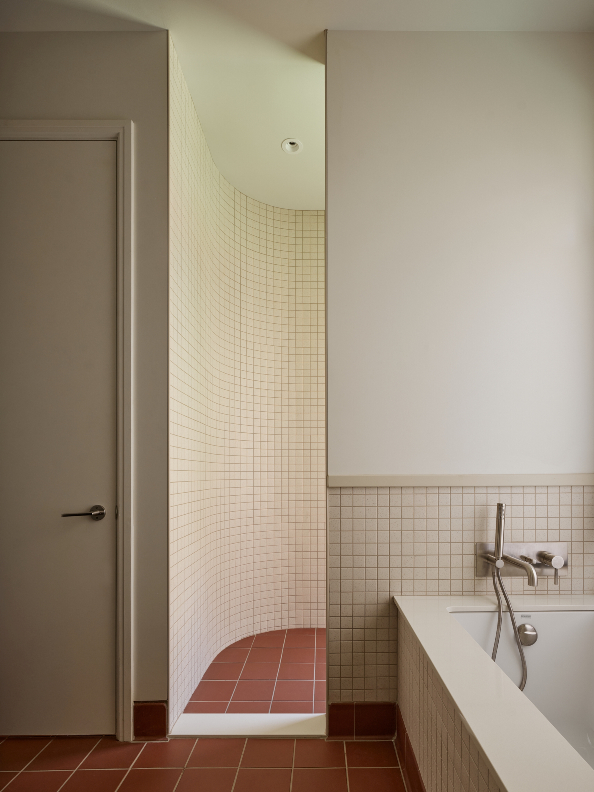 Curved shower alcove lined with small square tiles above terracotta floor tiles