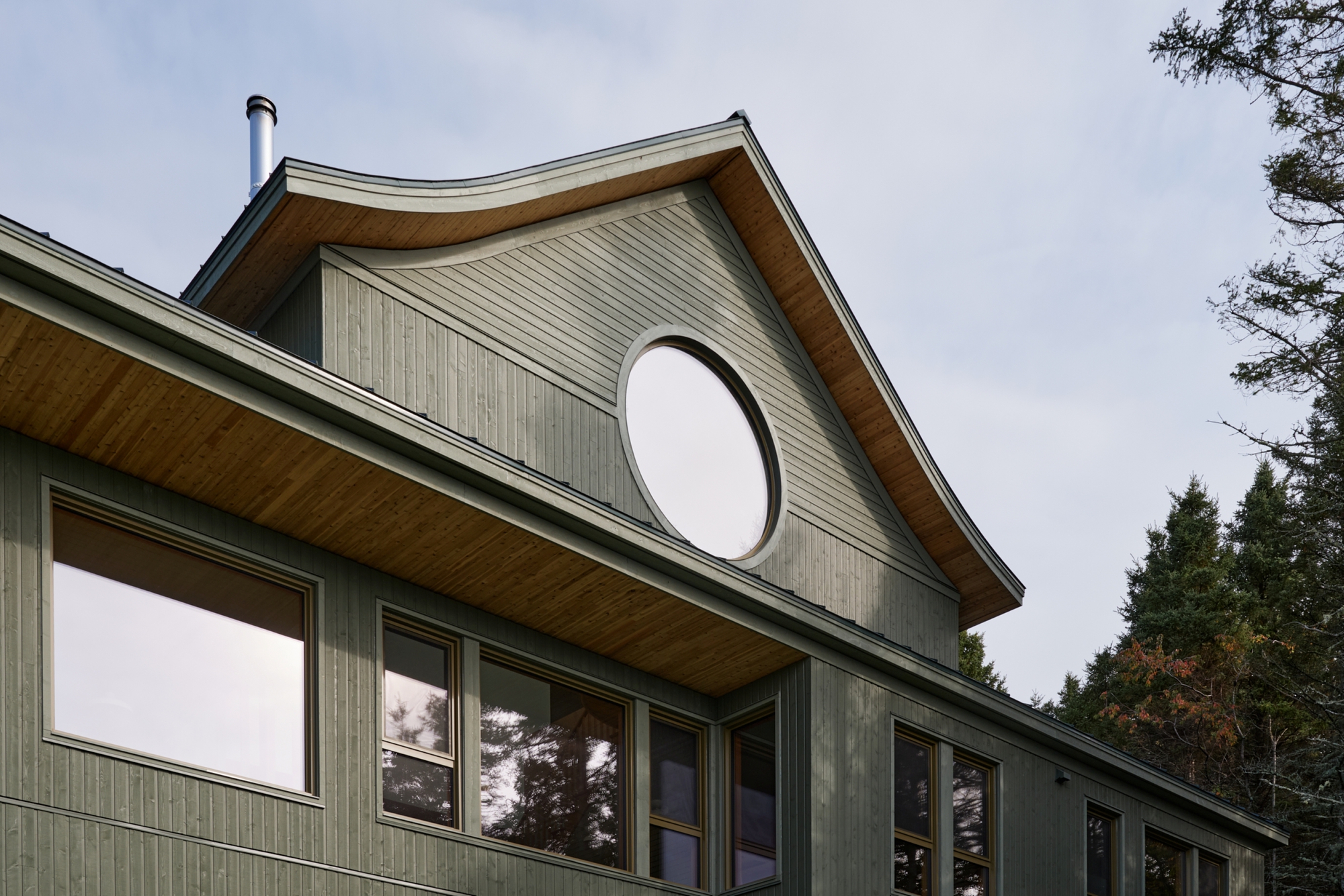 Gabled facade with vertical wood cladding and a large circular window in the upper gable