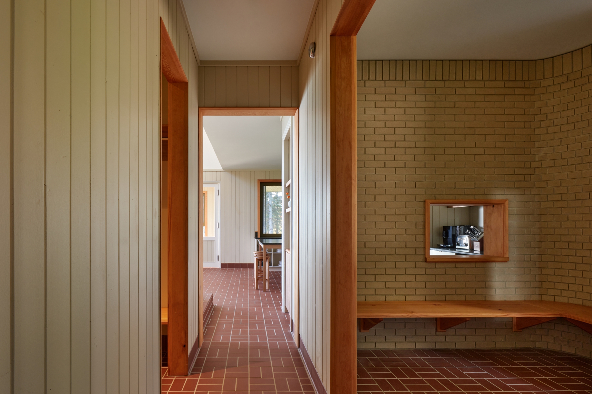 Corridor with vertical paneled walls, timber doorframes, and red brick herringbone flooring leading to adjoining rooms