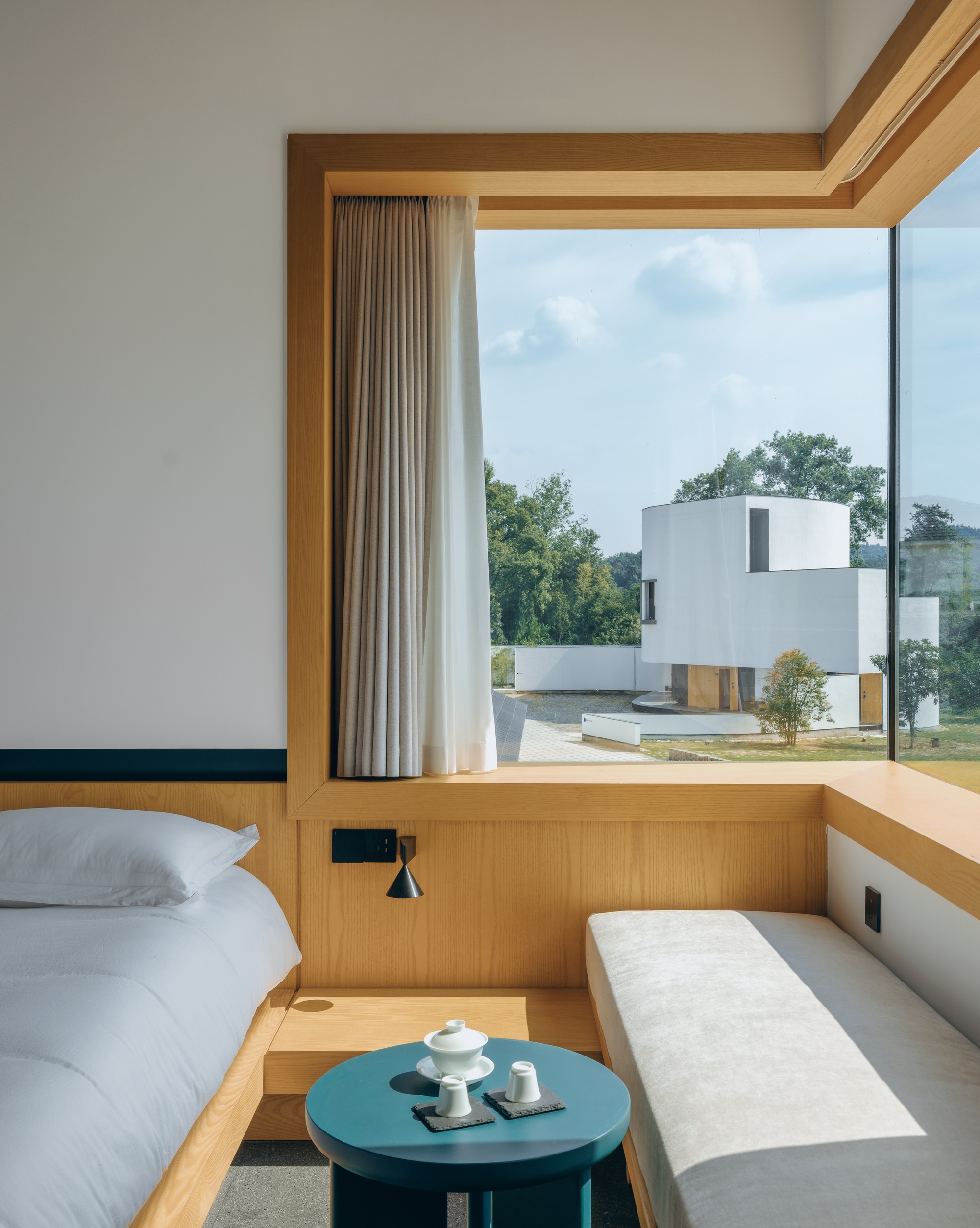 Guest room with timber-framed window seat and view to adjacent white geometric volume