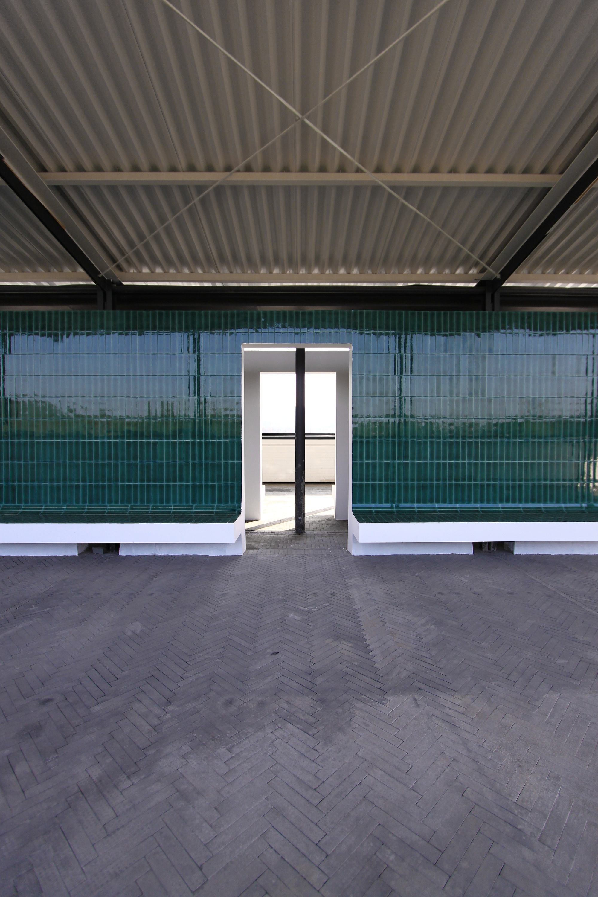Interior space with herringbone floor, corrugated metal ceiling and glazed tile walls flanking a central doorway