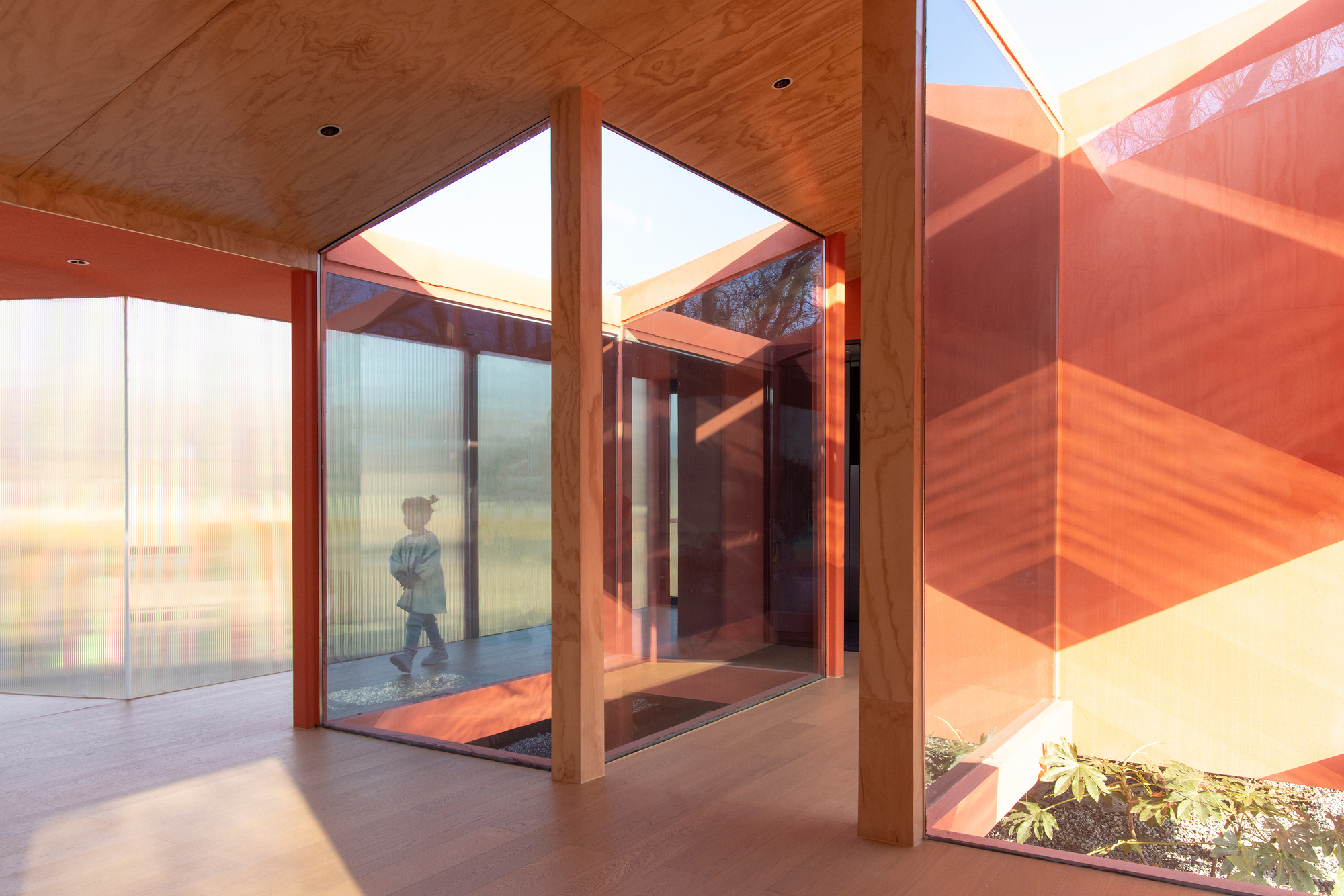 Interior entry corridor with timber-lined ceiling and glazed walls framing a child in translucent passage