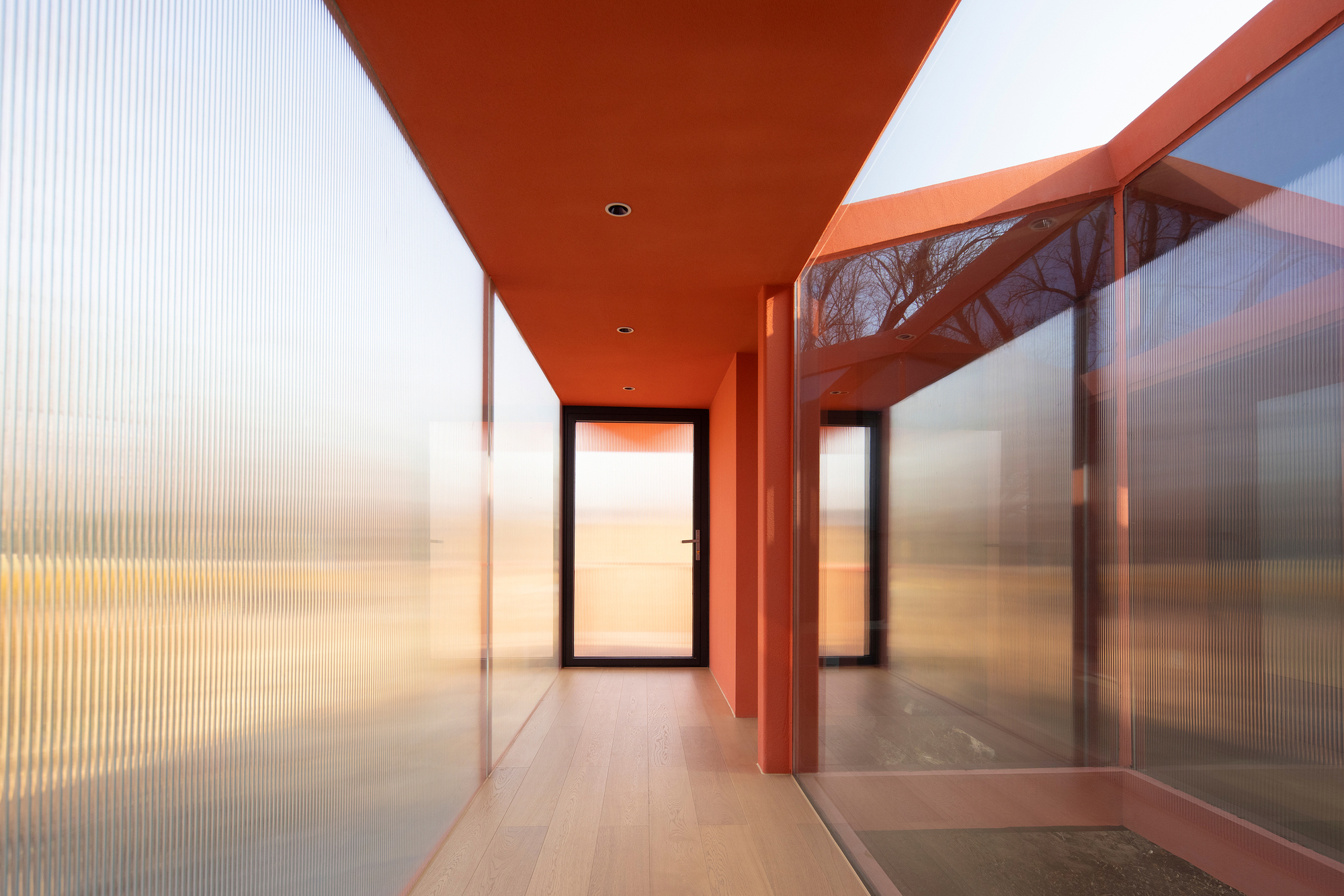 Corridor with translucent ribbed polycarbonate walls and orange ceiling leading to a glass door