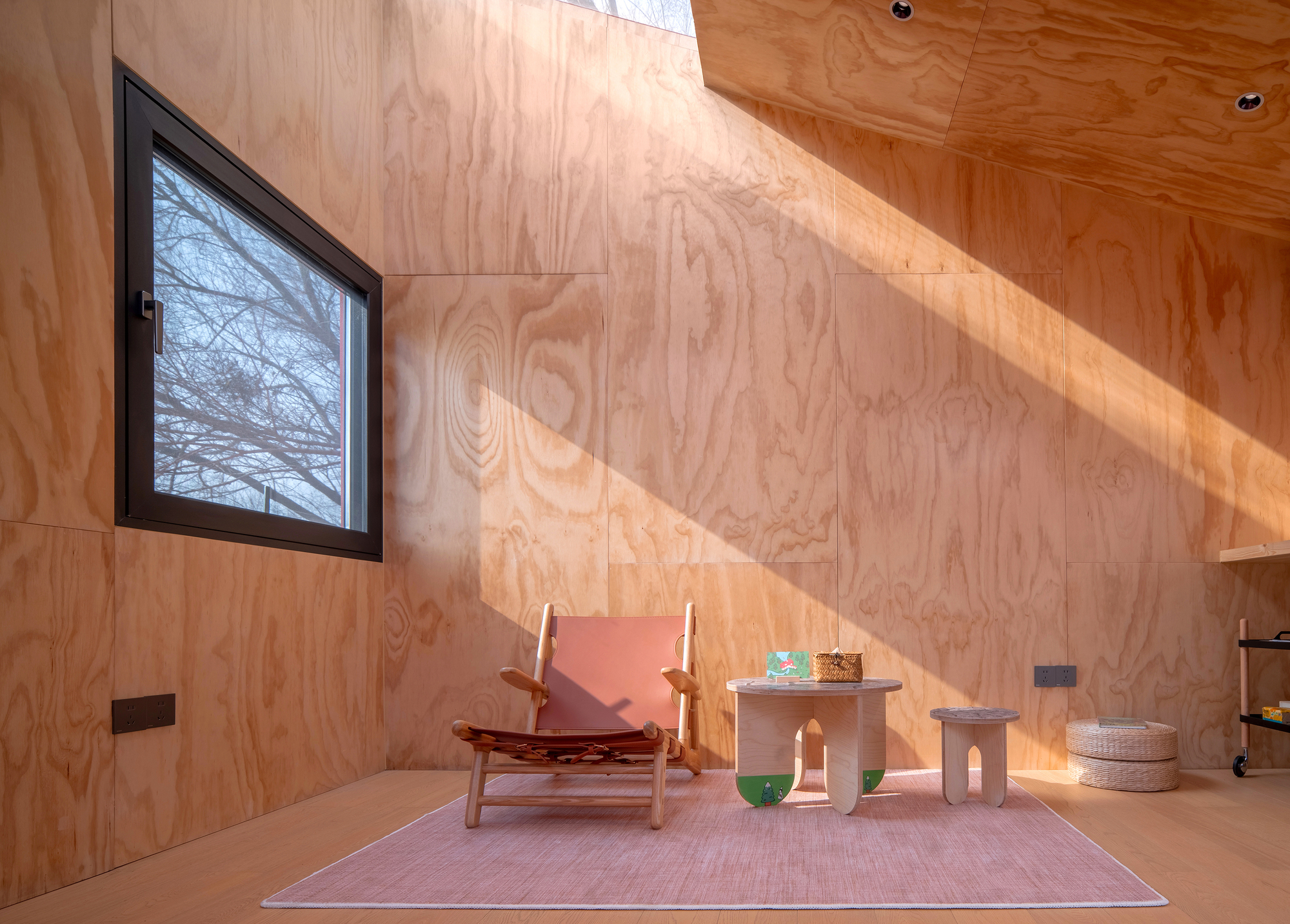 Plywood-clad sleeping nook with angled ceiling and square window framing bare winter branches