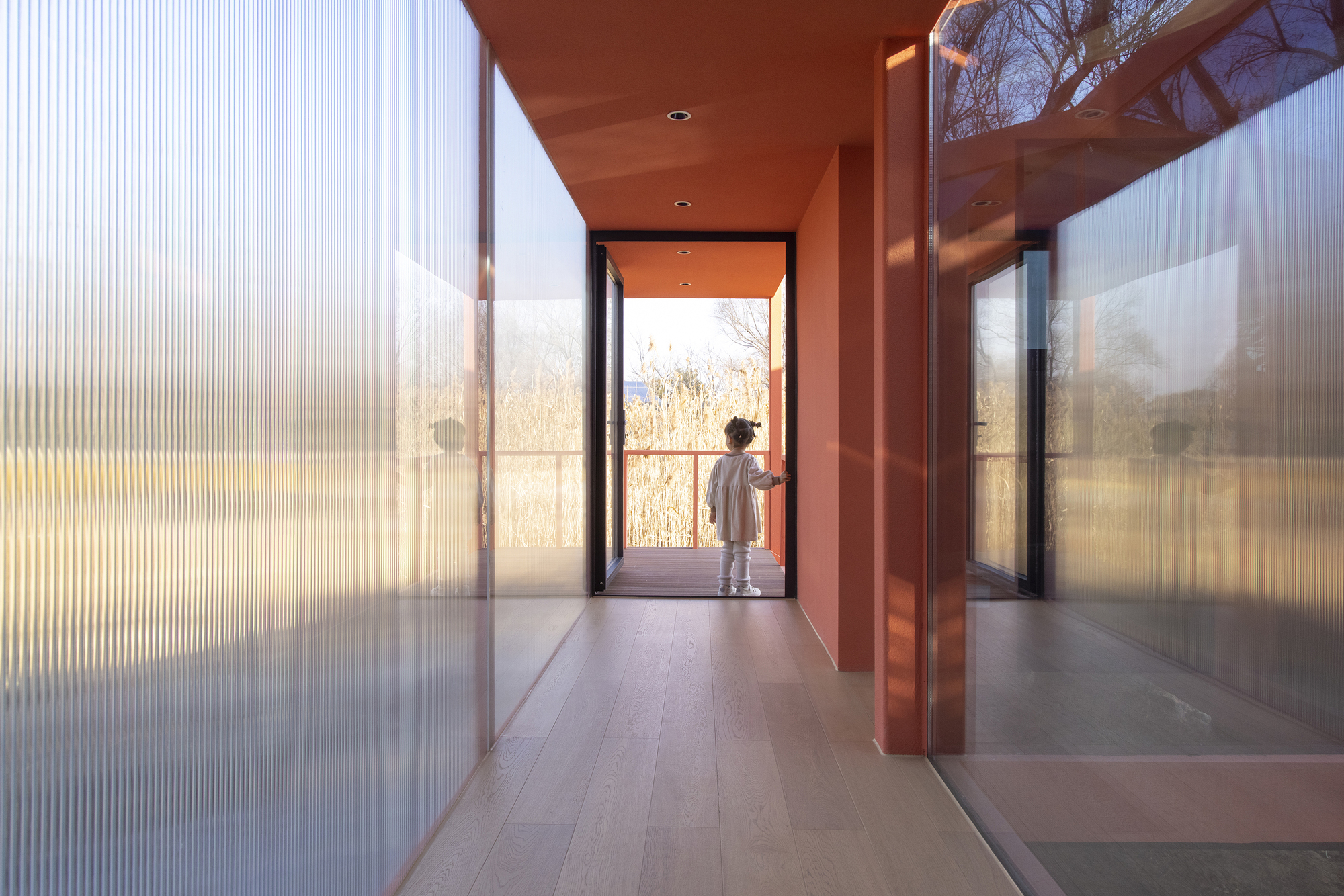 Interior corridor with fluted glass walls and a figure silhouetted in the doorway to the landscape