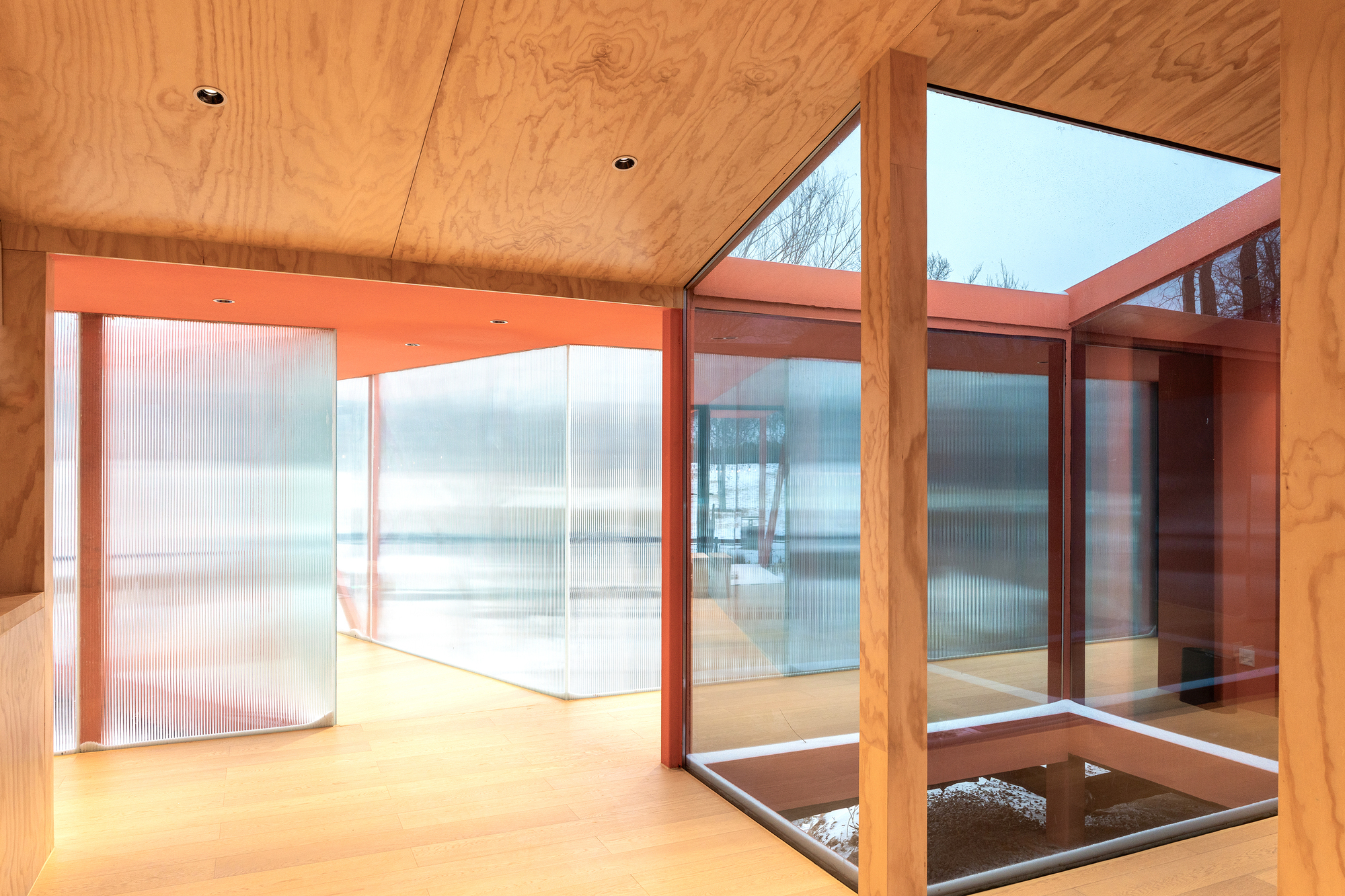 Interior corner with plywood ceiling and translucent corrugated wall panels framing a glazed courtyard