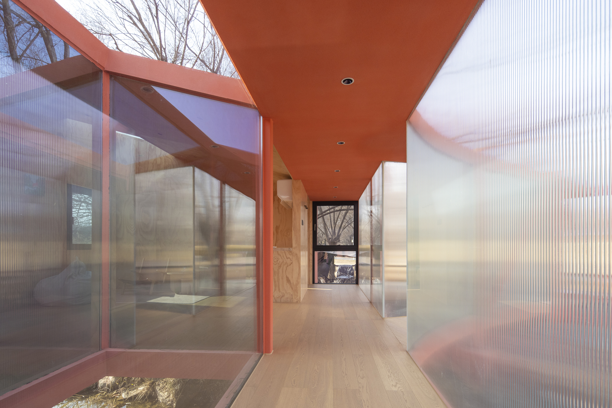 Corridor view with orange painted soffit and translucent corrugated walls flanking a planted courtyard