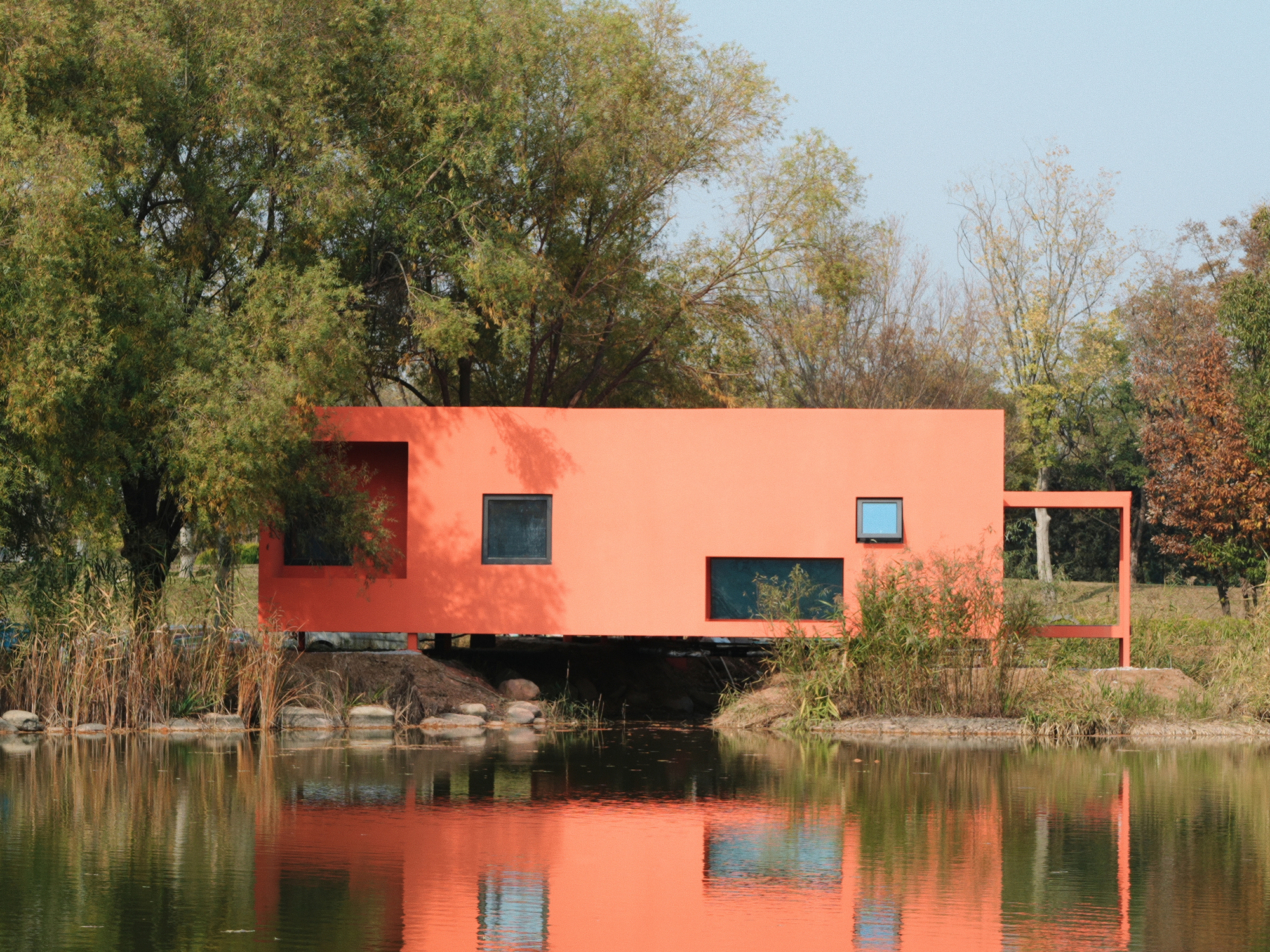 Lakeside elevation of the orange box volume on pilotis reflected in still water