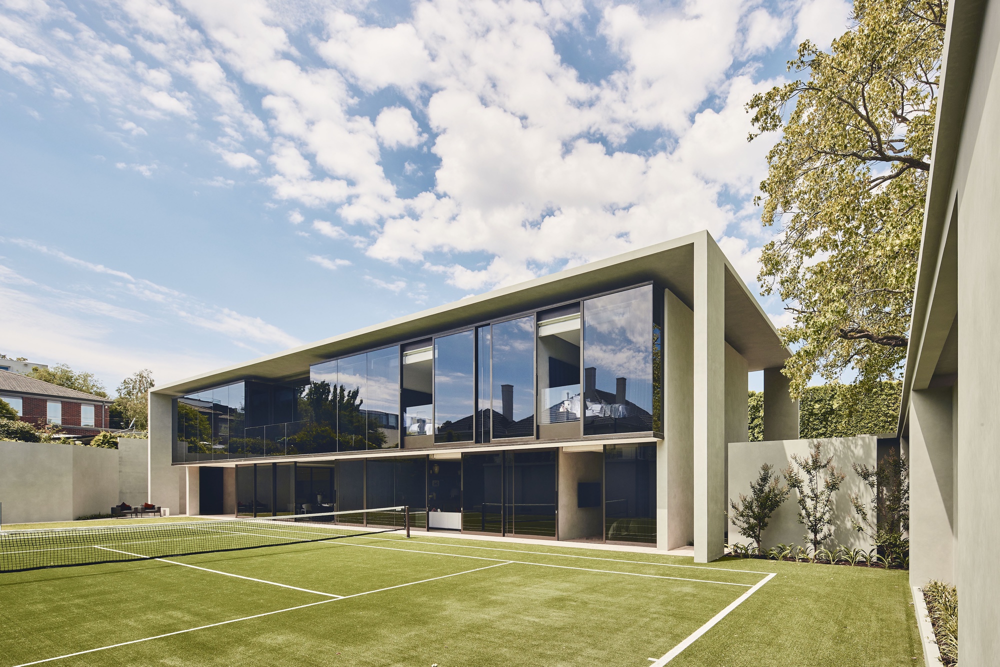 Rear elevation with floor-to-ceiling glazing overlooking a tennis court with synthetic grass surface