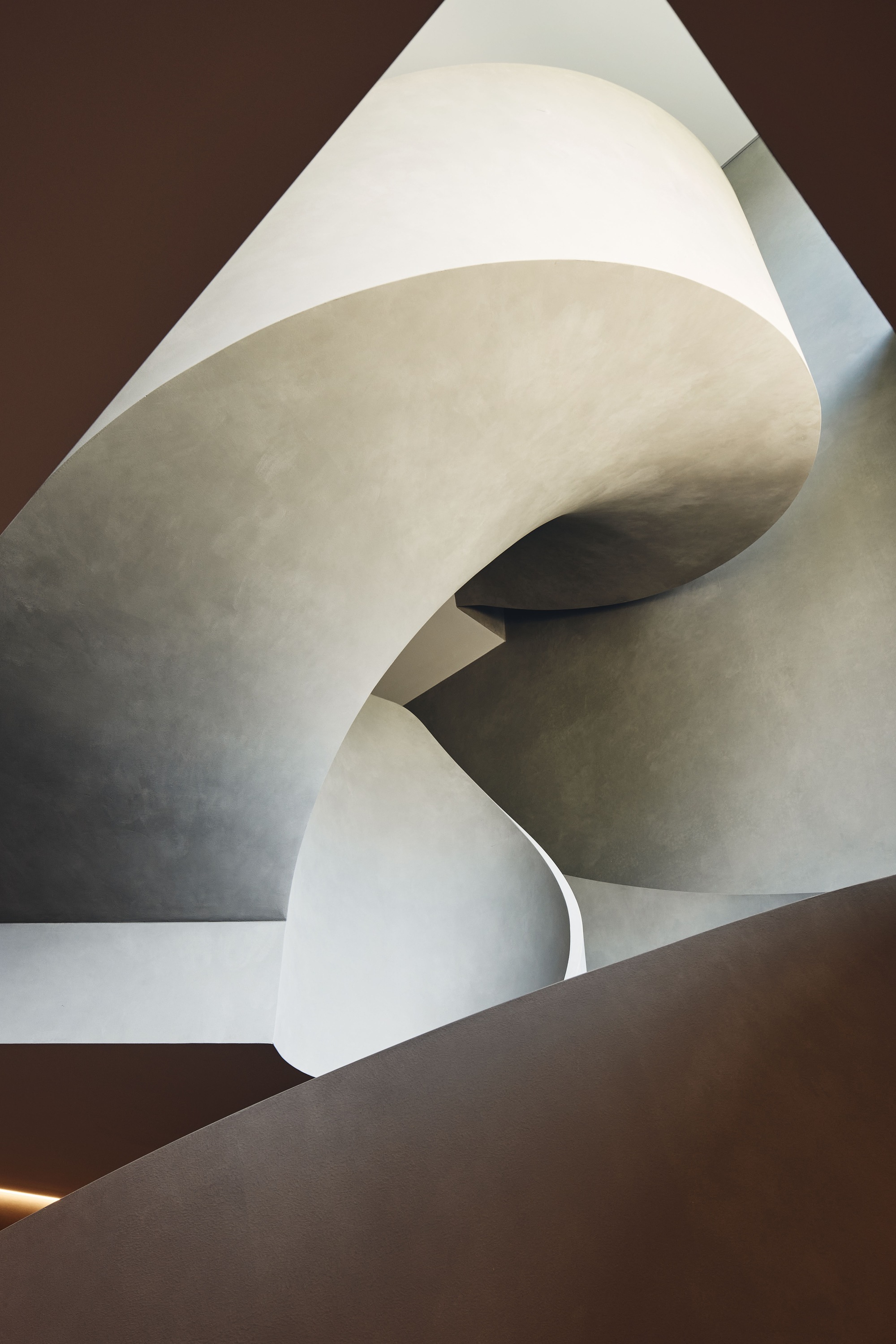 View upward through the stairwell showing layered curved plaster forms and shadow
