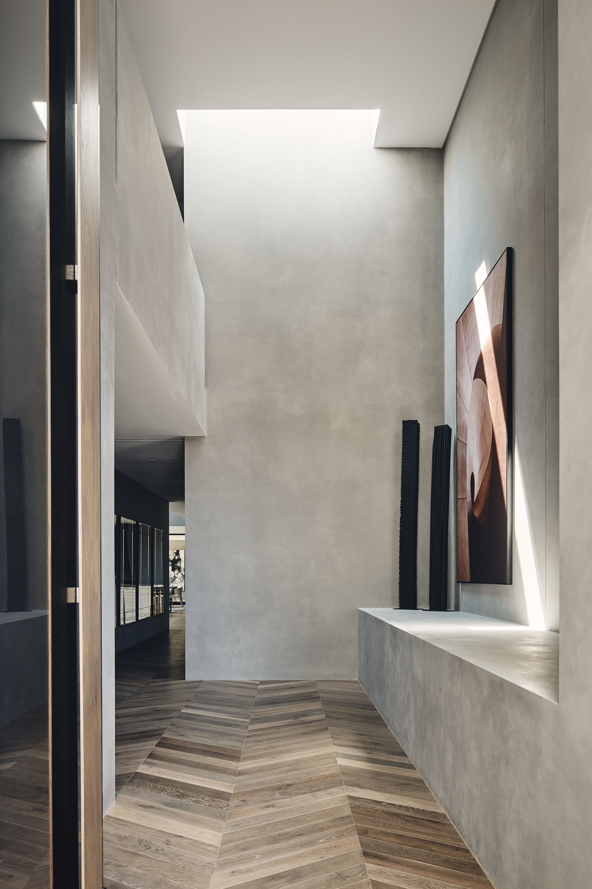 Corridor with herringbone timber floor, skylight above, and concrete bench displaying sculptures