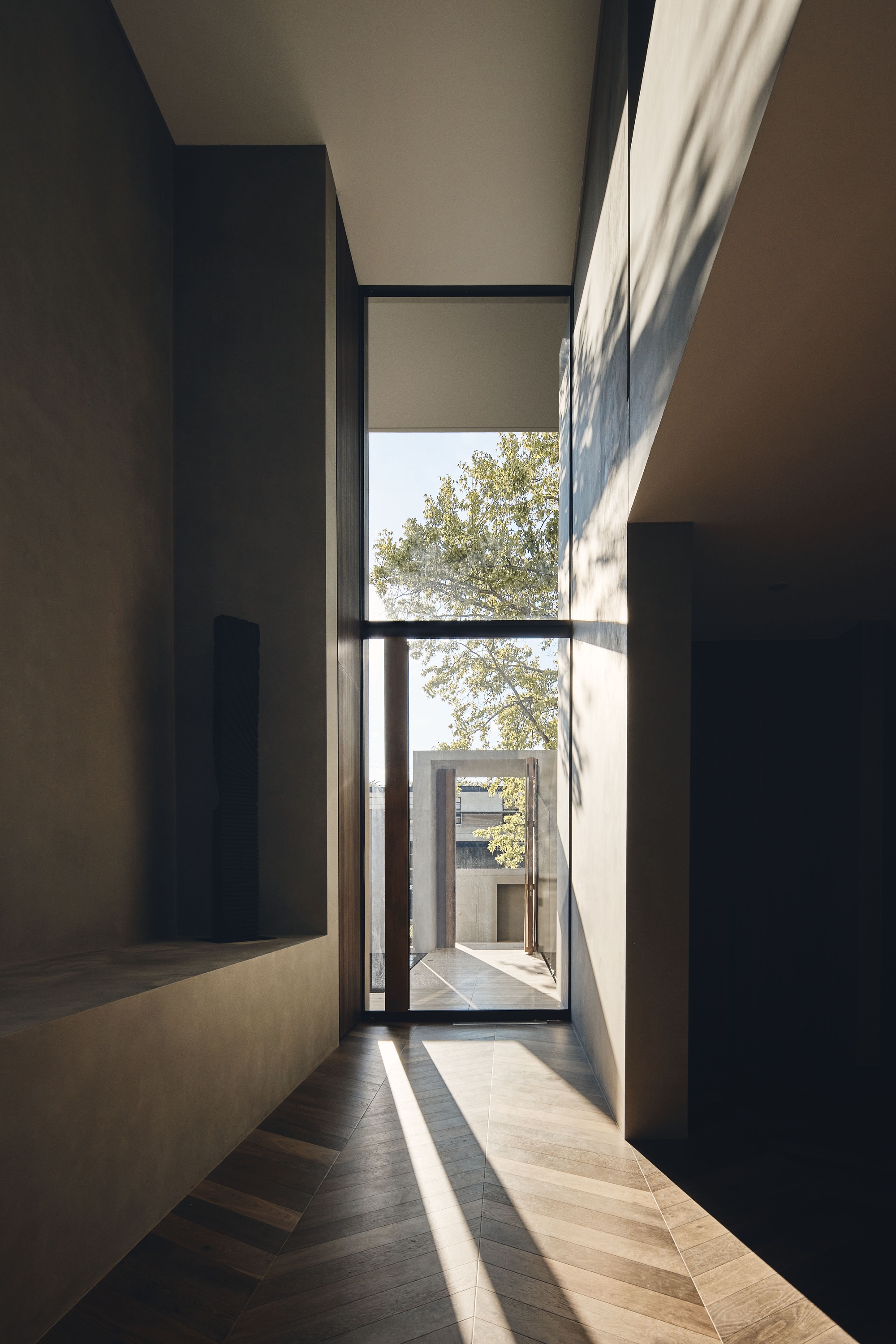 Hallway with tall glazed door framing a courtyard view and timber flooring in afternoon sun