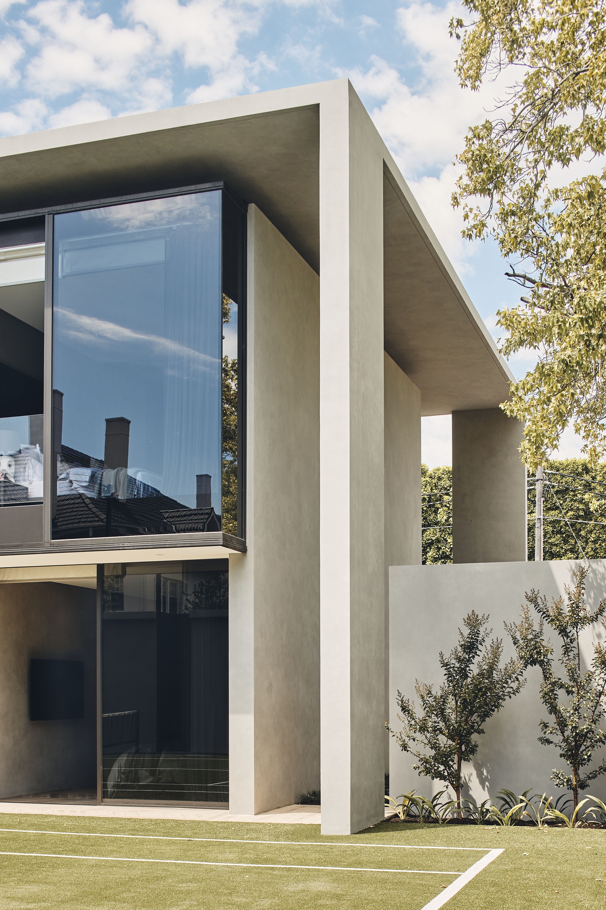 Exterior corner showing deep concrete frame around glazing with olive trees and lawn