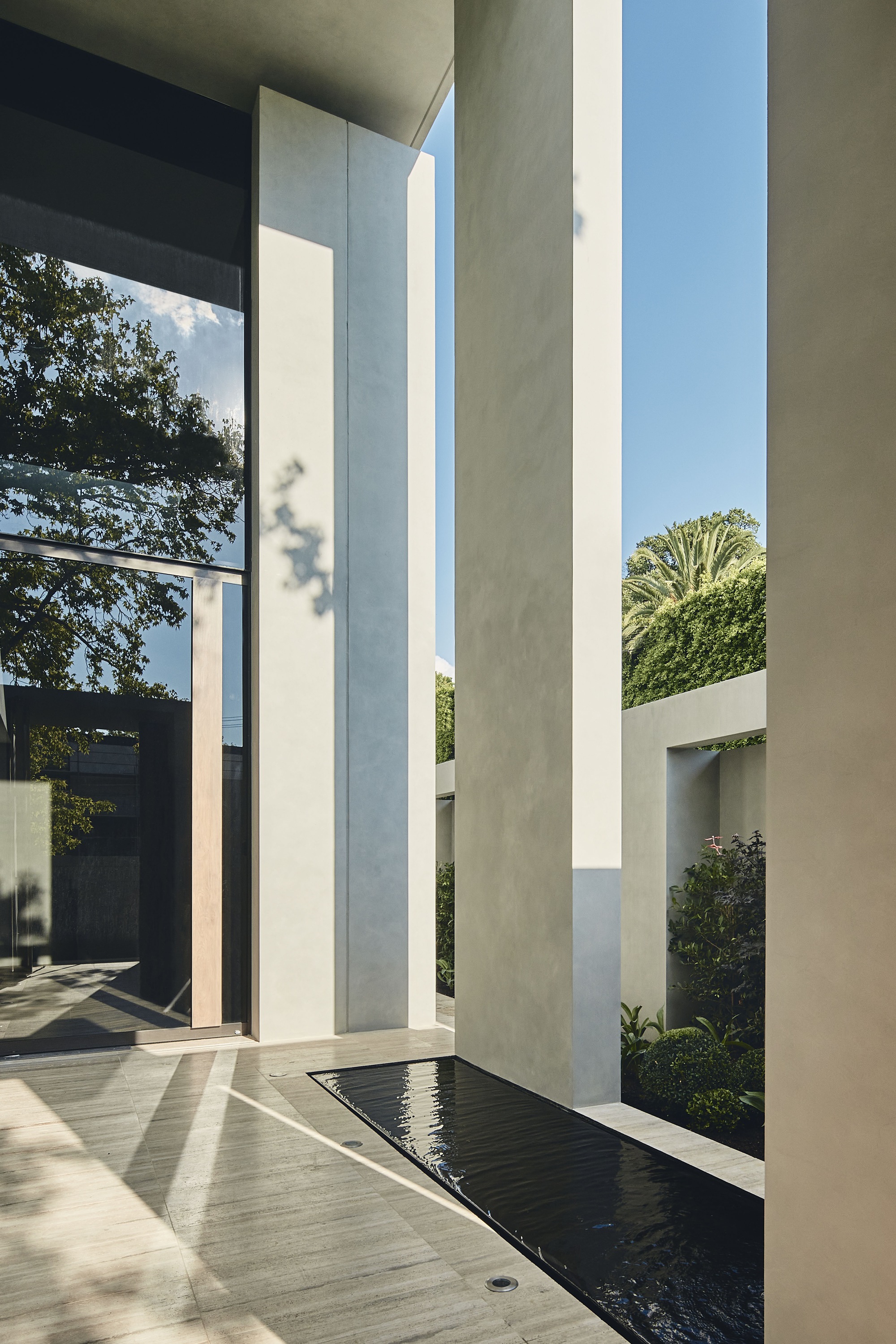 Concrete entry courtyard with tall vertical columns flanking a reflecting pool and planted beds