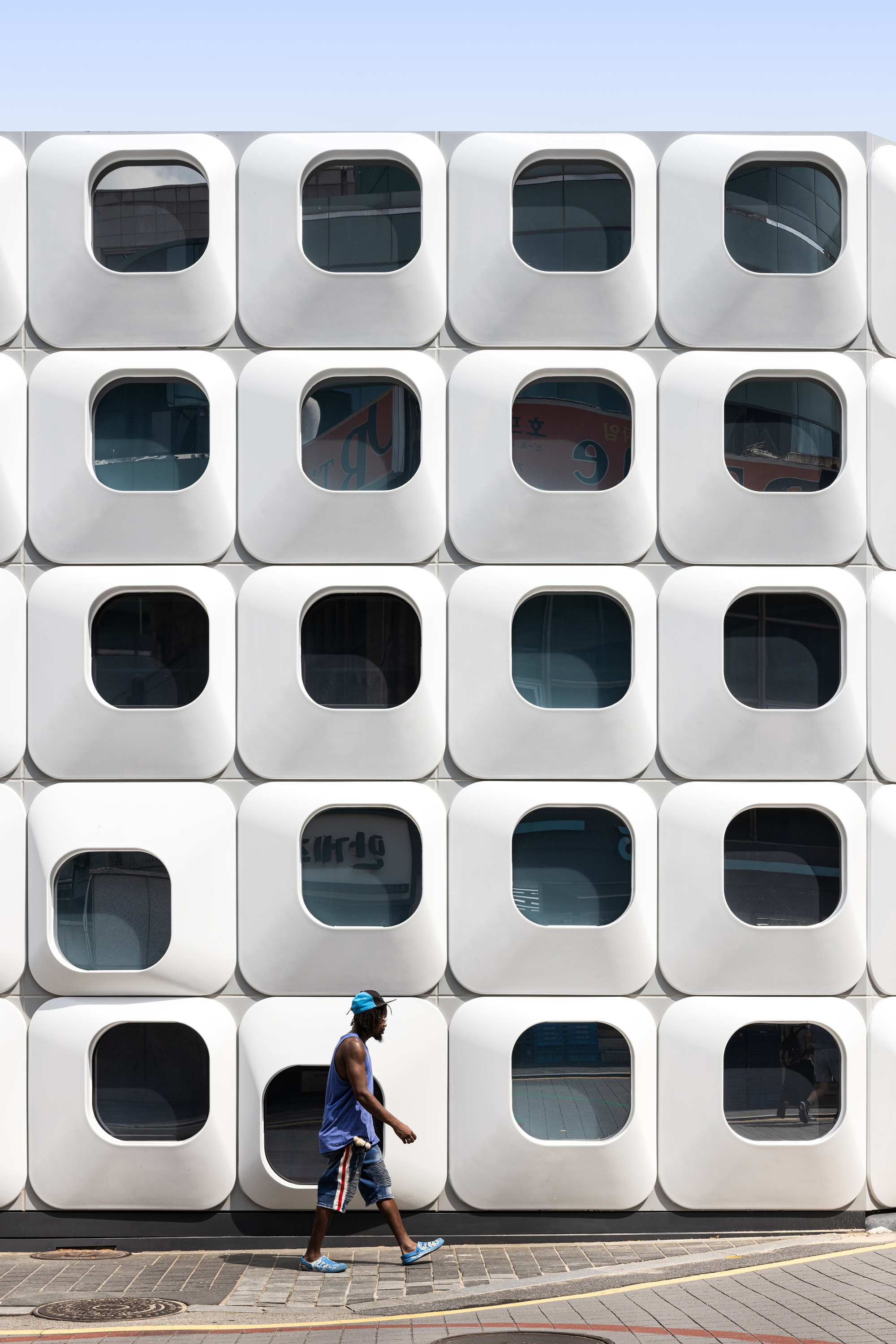 Grid of rounded square window modules with a person walking past on the pavement below