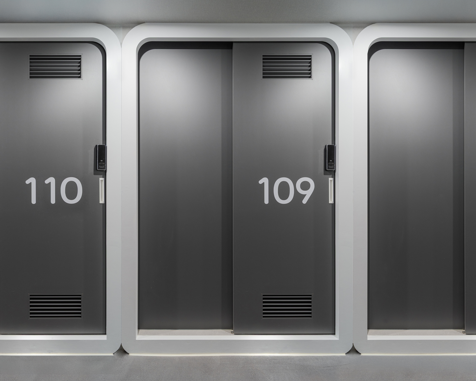 Row of numbered grey sliding doors with ventilation grilles and white rounded frames