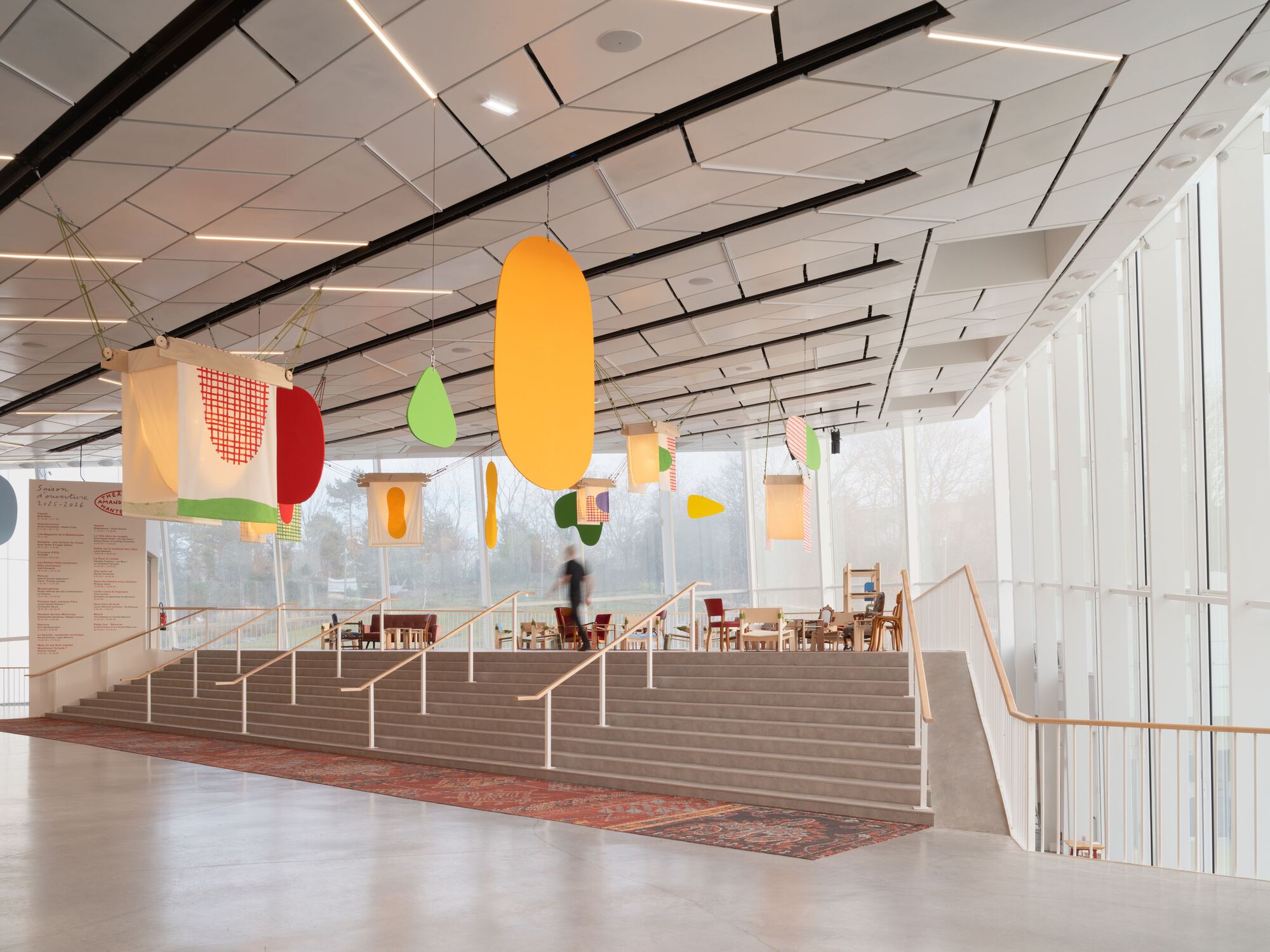 Wide timber staircase with metal railings beneath geometric ceiling and colorful hanging banners