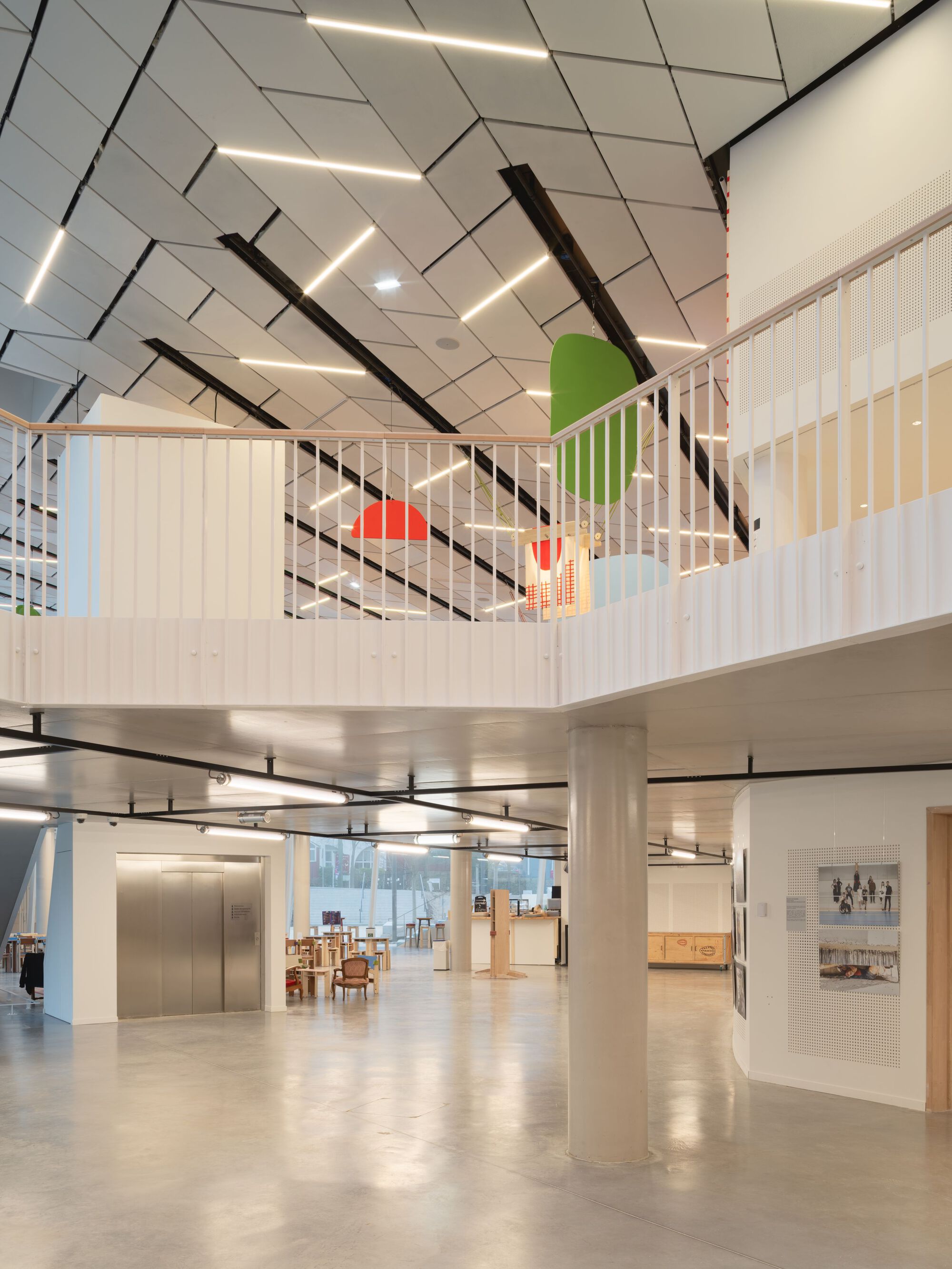 Interior atrium looking up to mezzanine with vertical slat railings and angular white ceiling panels