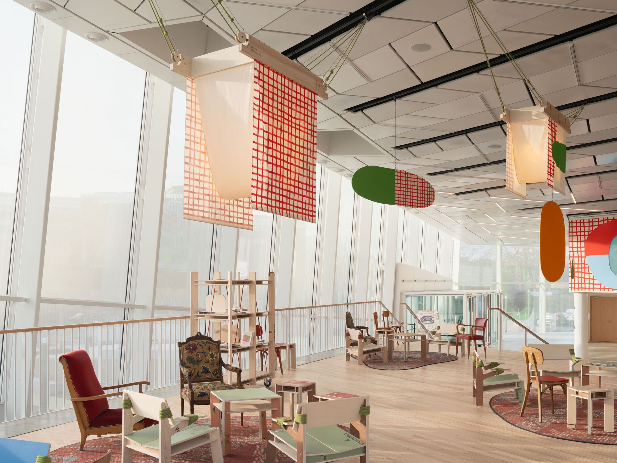 Interior space with hanging fabric panels in orange and green tones beneath a faceted white ceiling