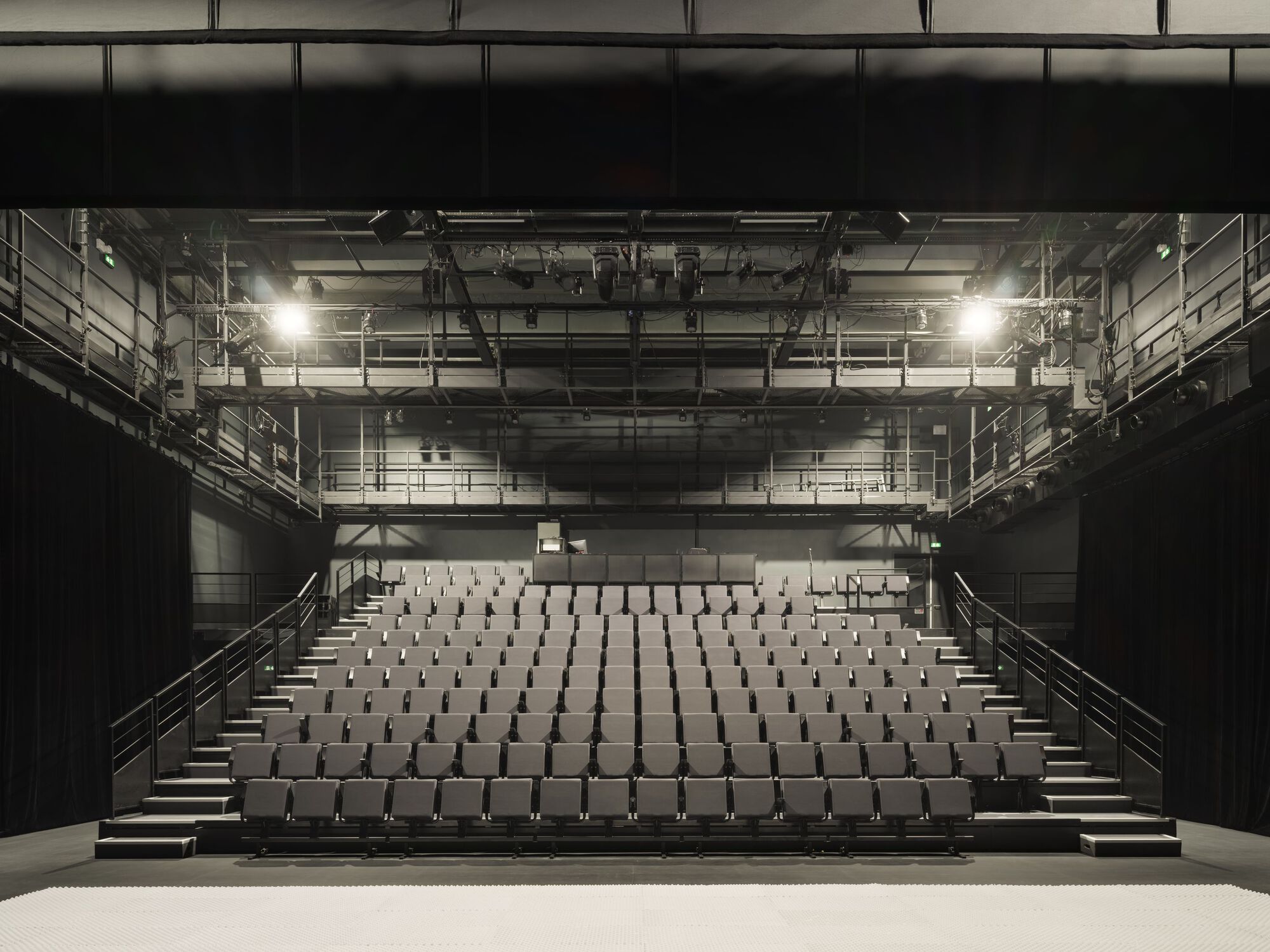 Frontal view of the theatre auditorium with tiered seating and exposed lighting rigging overhead