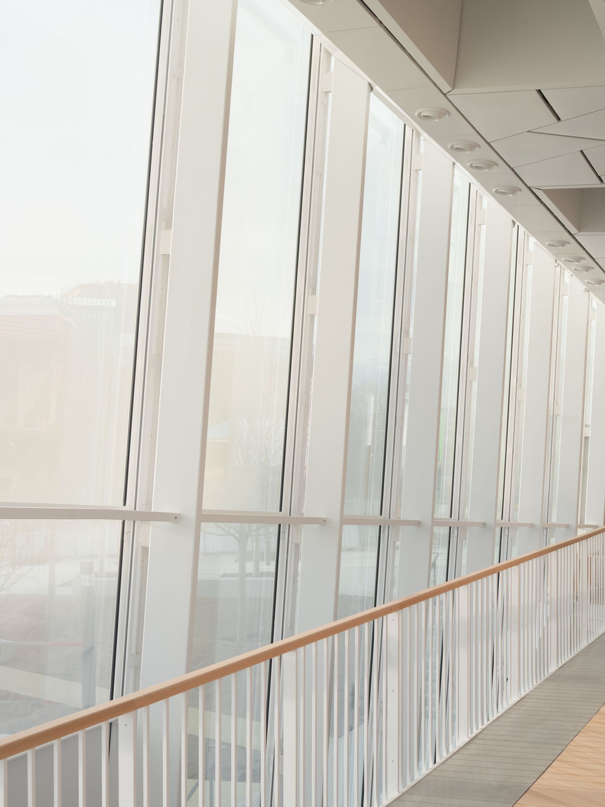 Corridor with floor-to-ceiling glazing and vertical white balusters in overcast daylight
