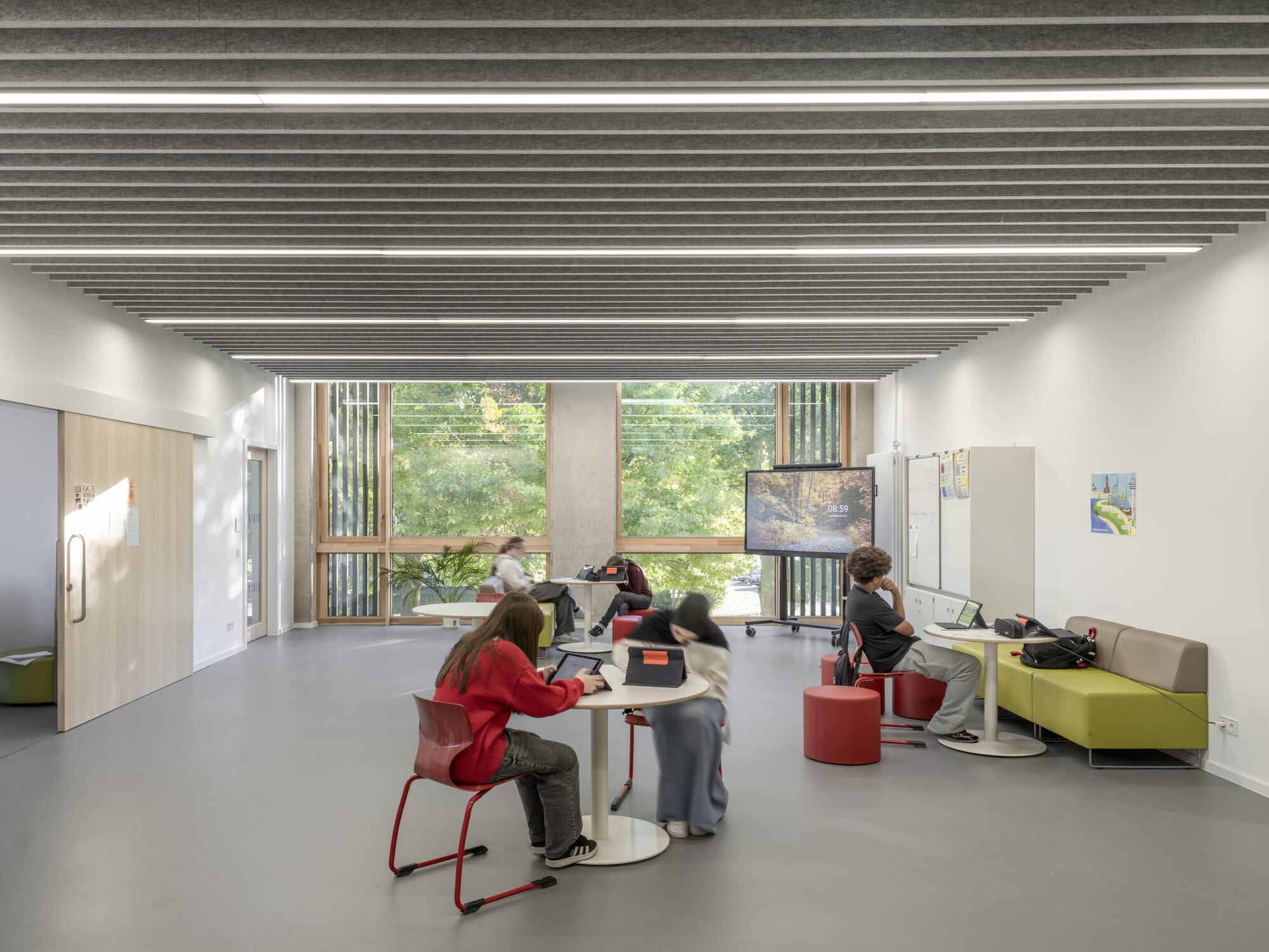 Classroom with slatted ceiling baffles, a window to greenery and students at low tables