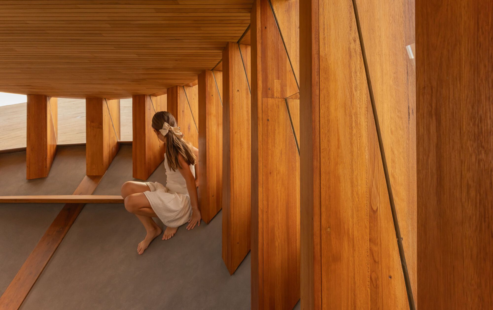 Angled timber wall panels and built-in bench seating with grey concrete floor and seated figure