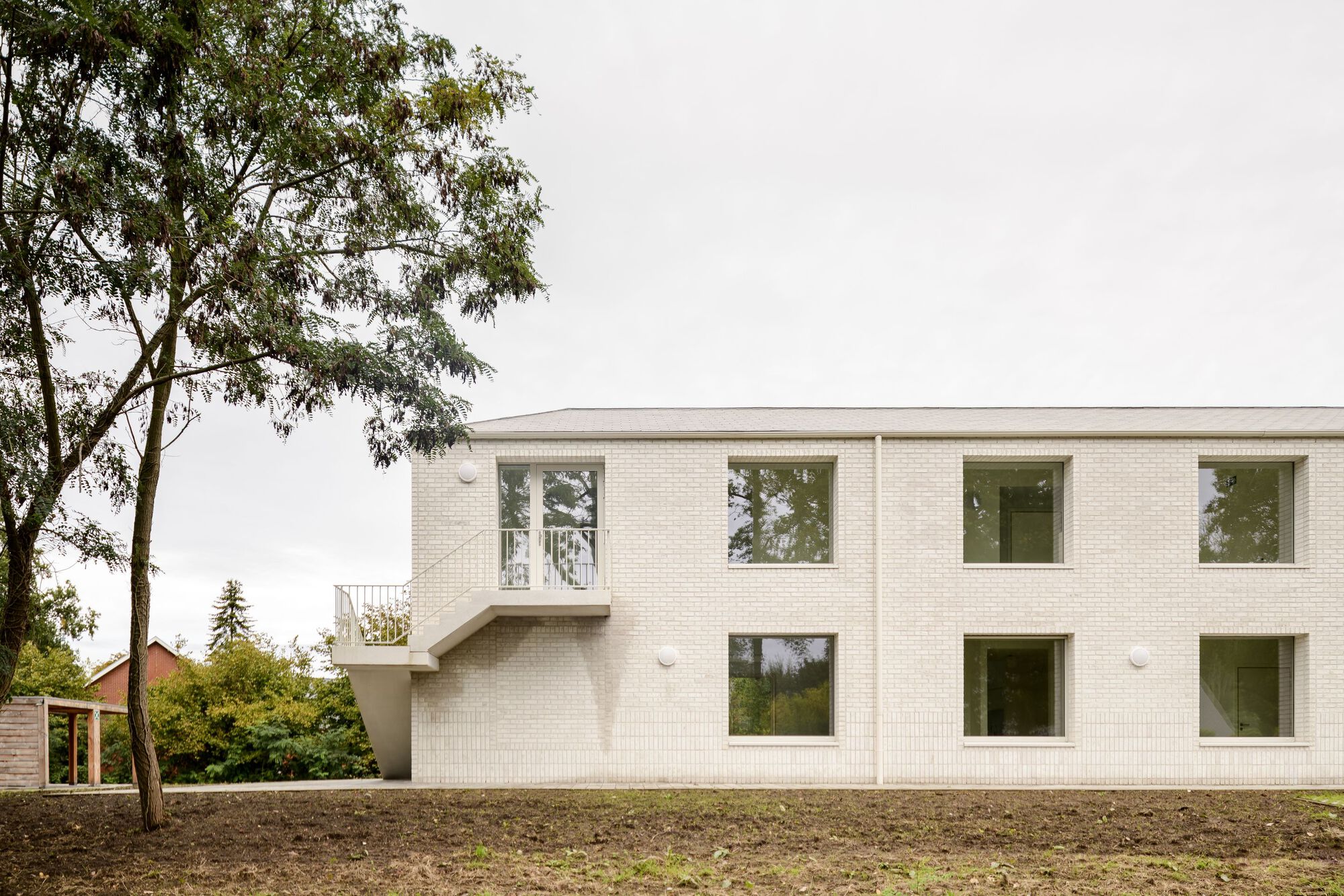 White brick facade with offset windows and cantilevered bay framed by a leafy tree