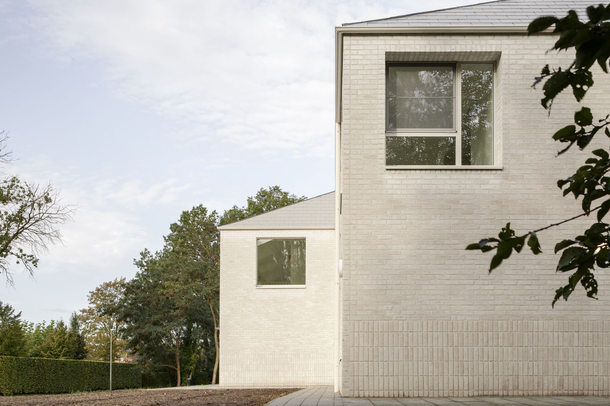 White brick facade with pitched roof and vertically ribbed base beneath overcast sky