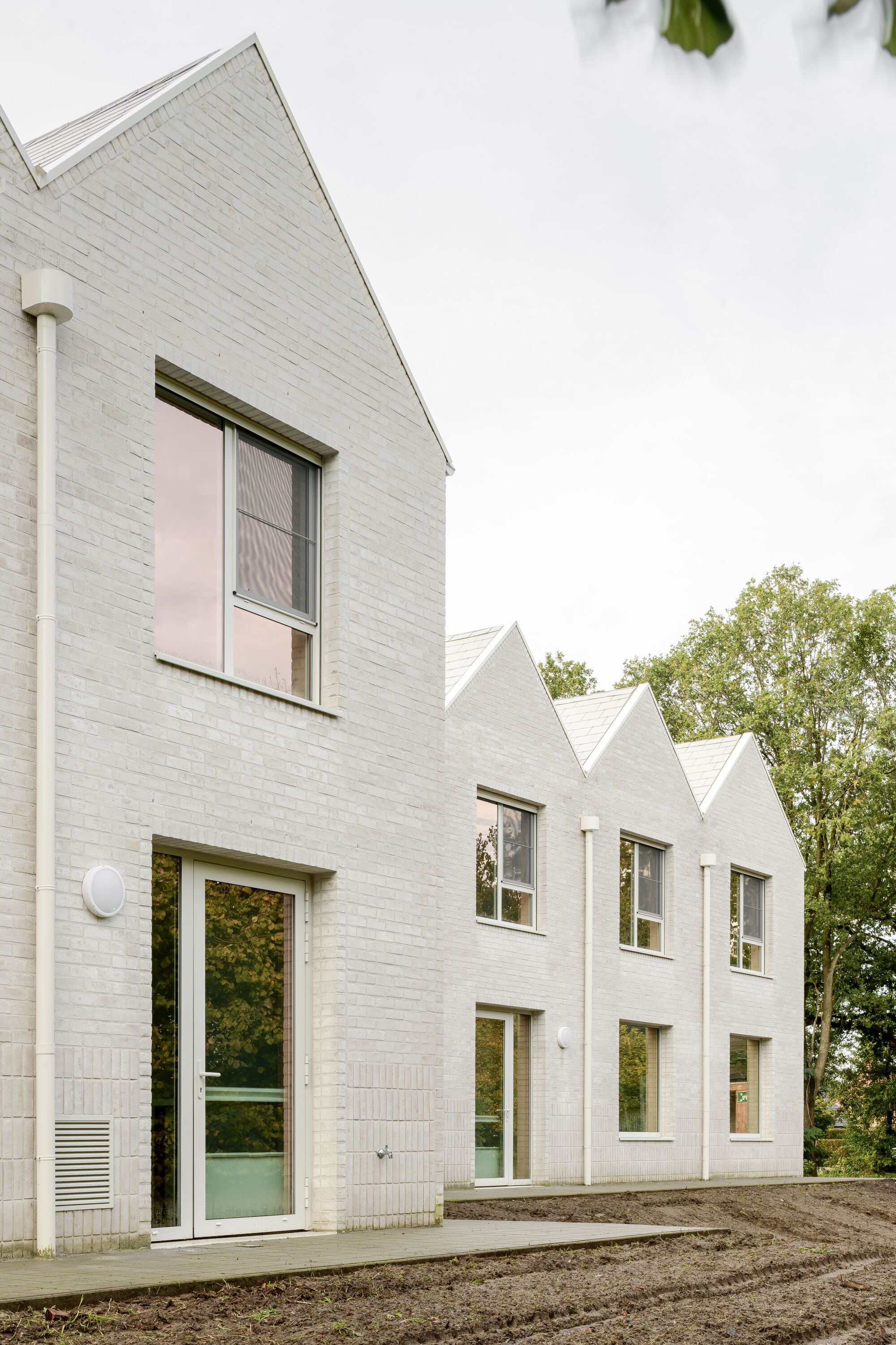 Row of white brick gabled volumes with glazed doors and unpaved earthen foreground