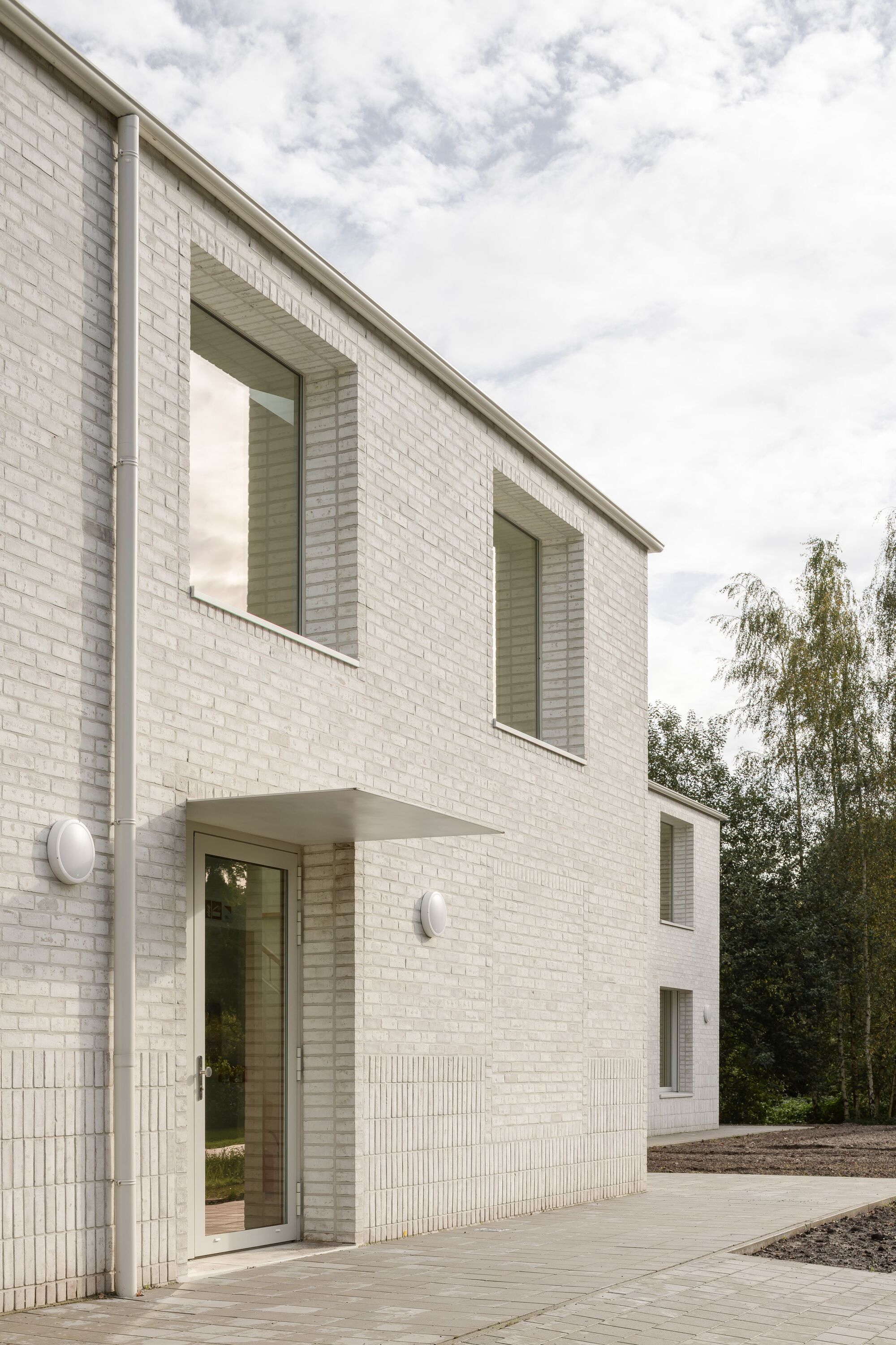 Recessed entrance with cantilevered canopy flanked by vertically ribbed brick panels under cloudy sky