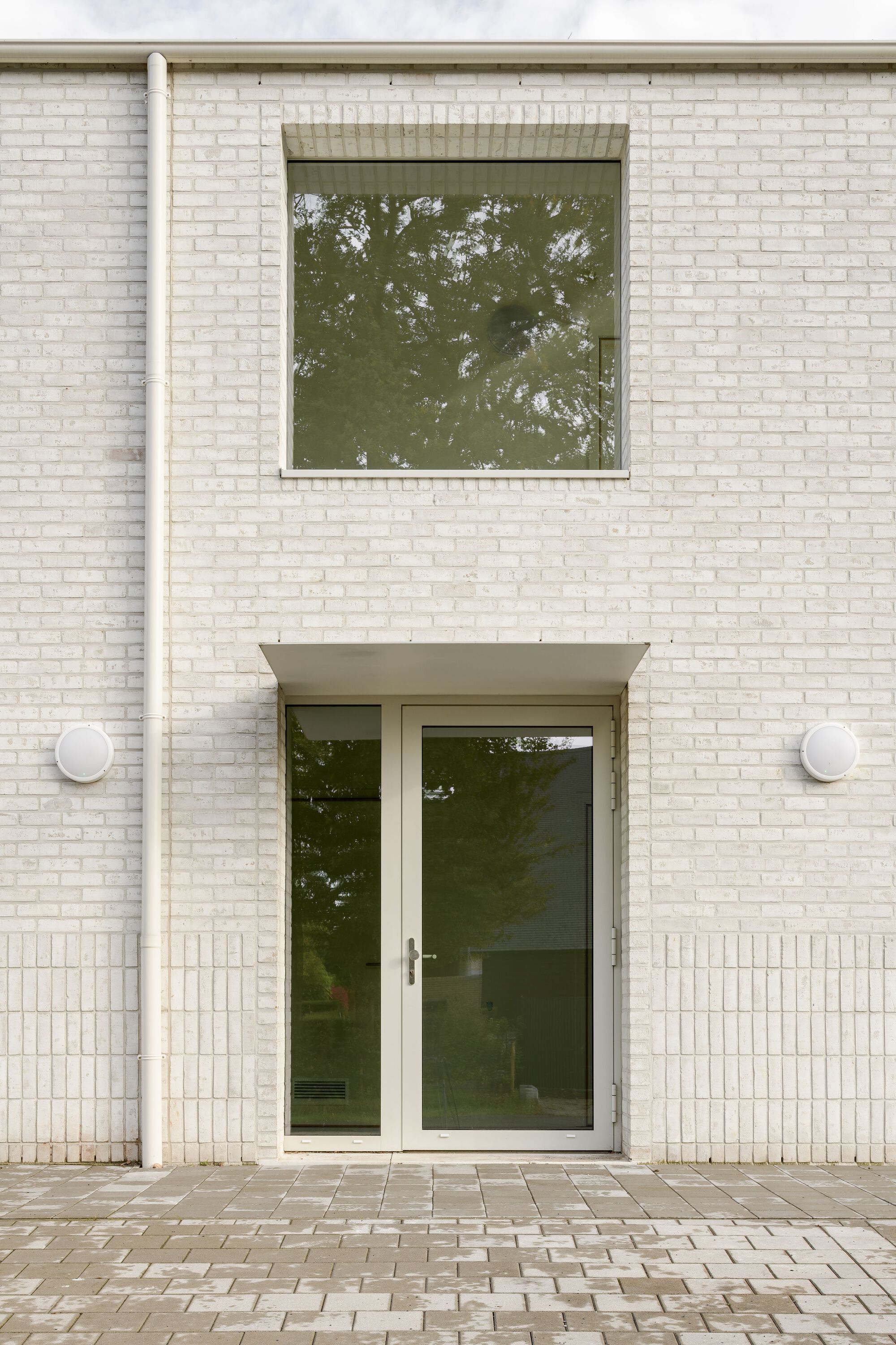 Front entry with glass door beneath canopy and square window on white brick facade