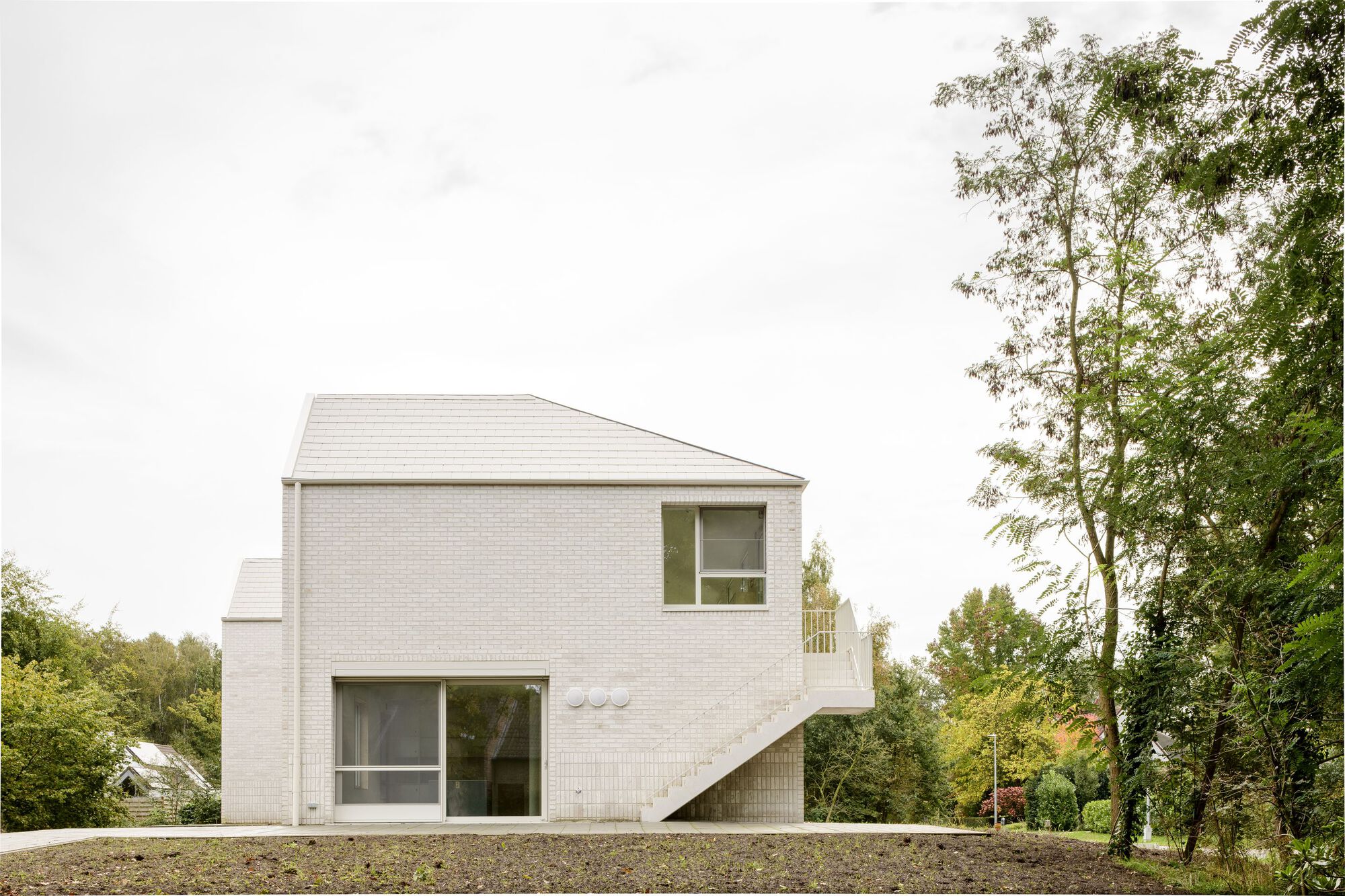 Pale brick facade with external staircase and gravel site under overcast sky