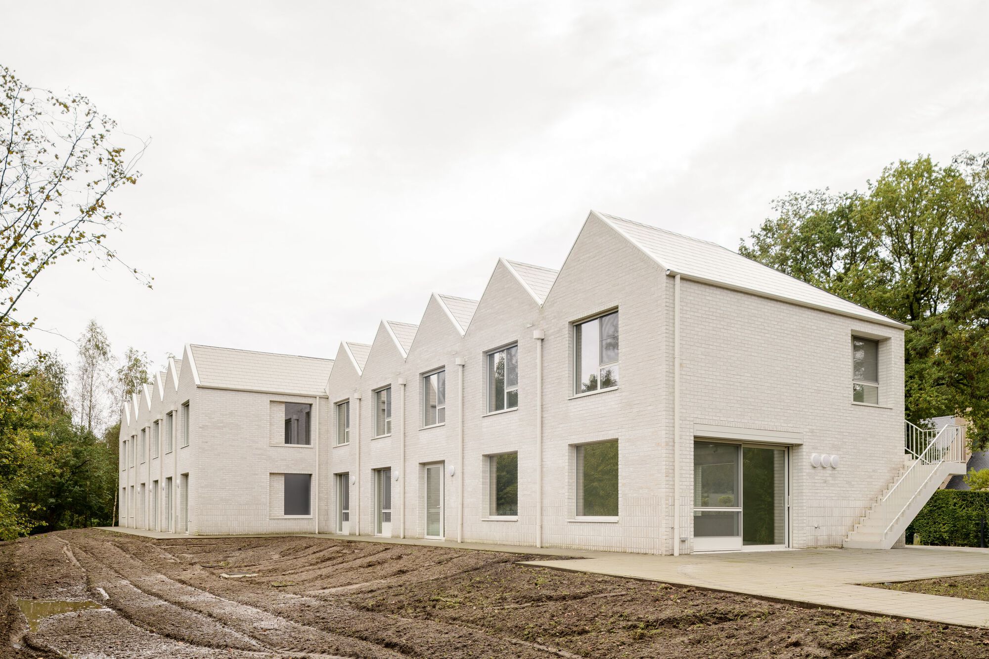 Longitudinal view of repeating gabled volumes in pale brick with freshly graded earth
