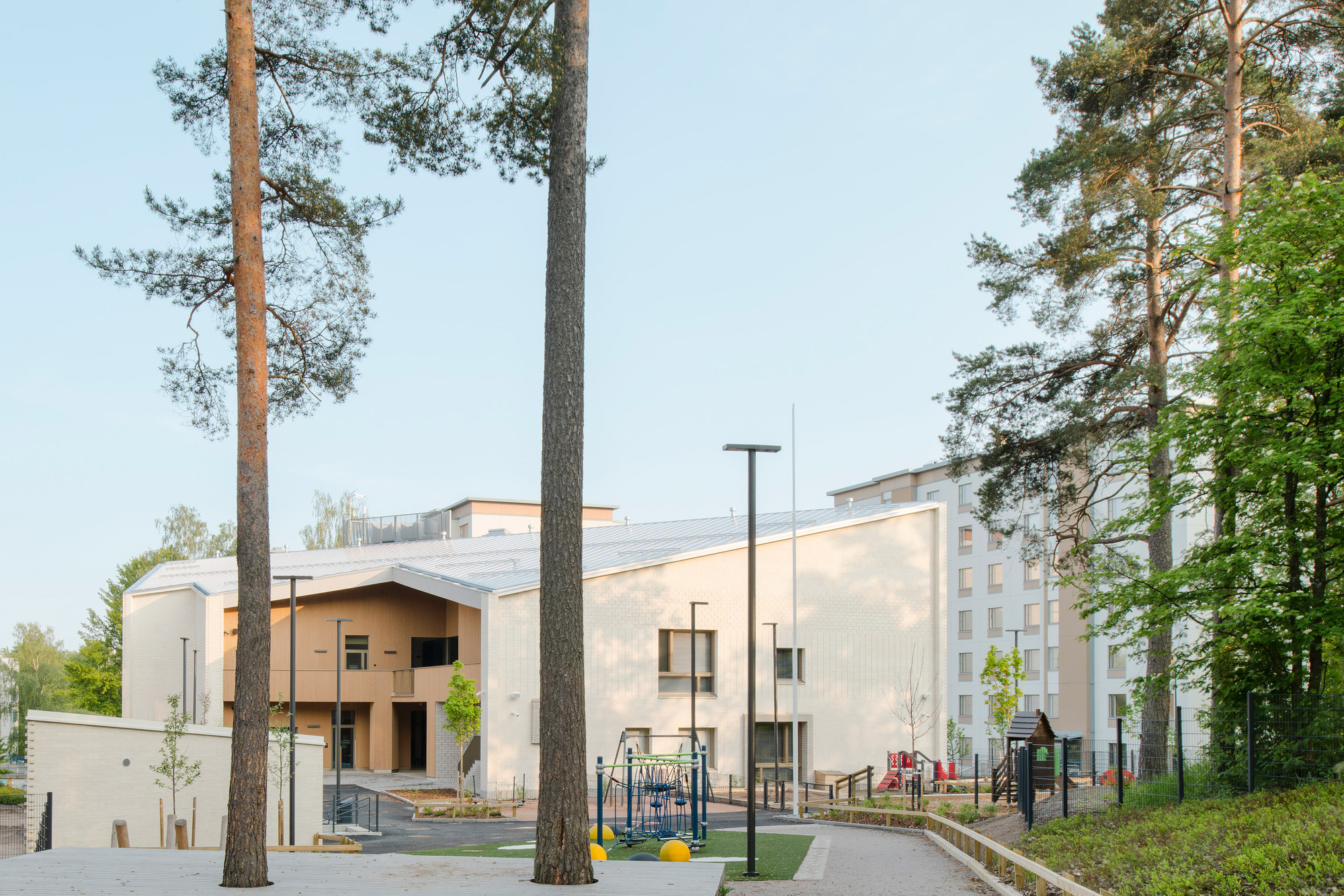 Pale metal-clad volumes with a central courtyard seen through tall pine trees at dusk