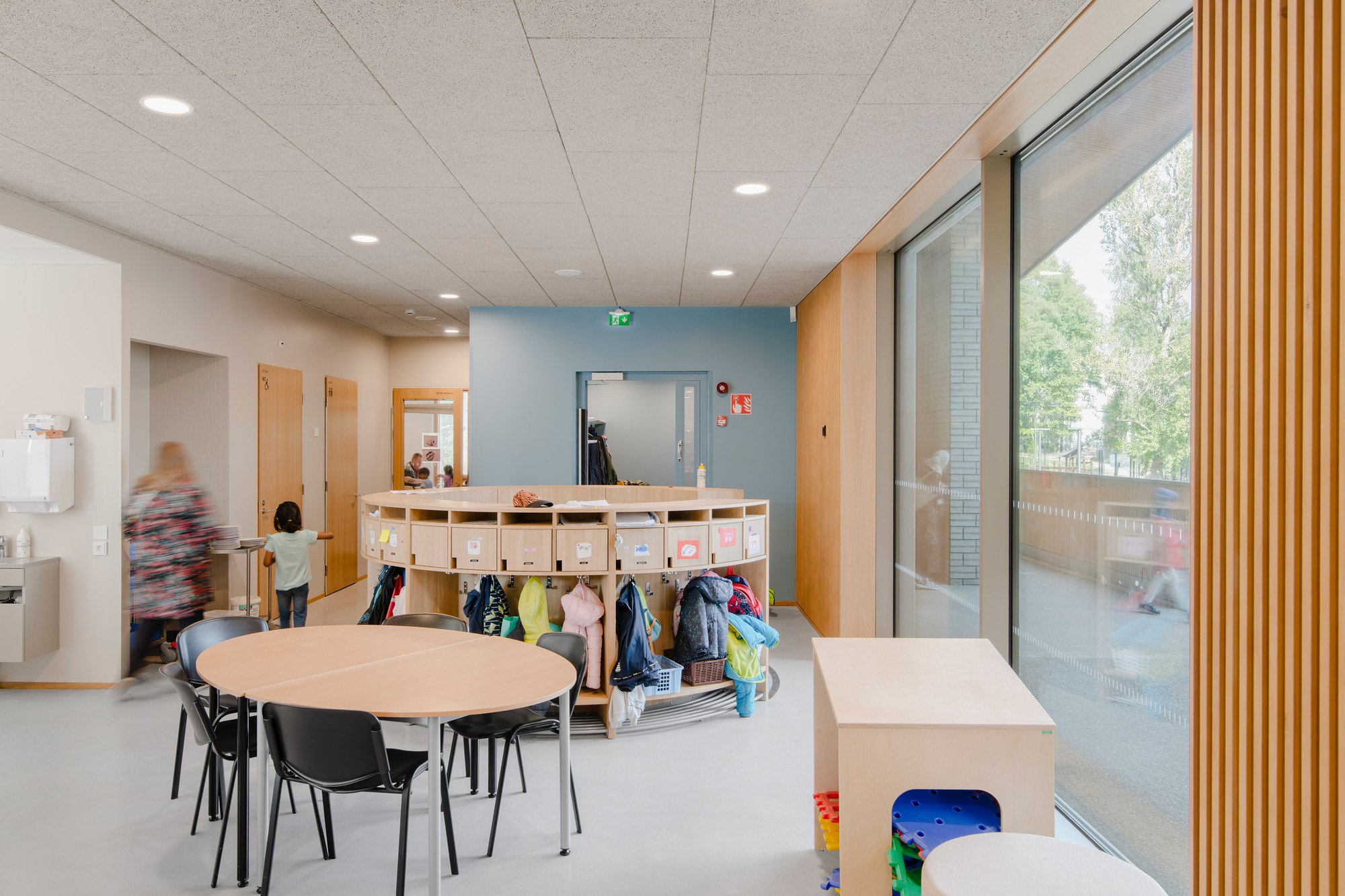 Classroom interior with blue accent wall, storage cubbies, round tables and a timber slat screen